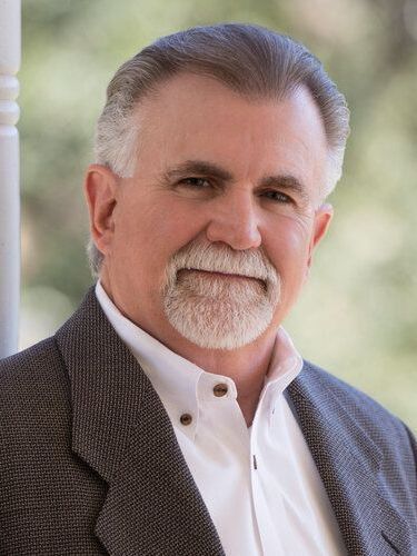 A man with a beard is wearing a suit and white shirt.