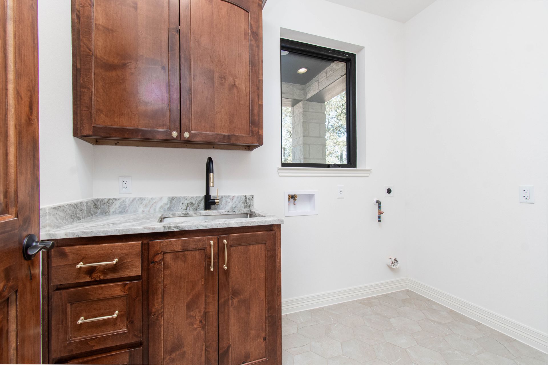 A laundry room with wooden cabinets , a sink , and a window.