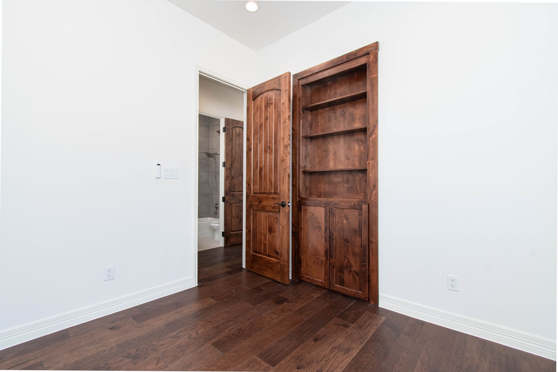A bedroom with hardwood floors and two wooden doors.