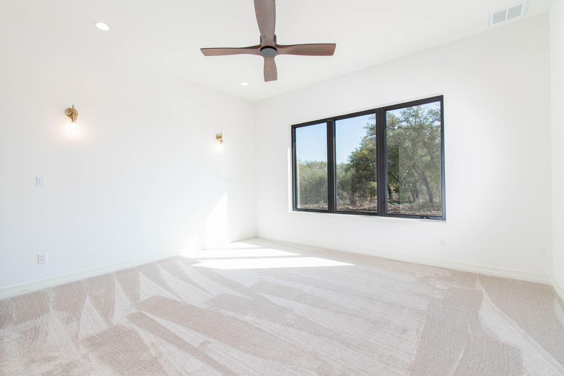 An empty bedroom with a ceiling fan and three windows.