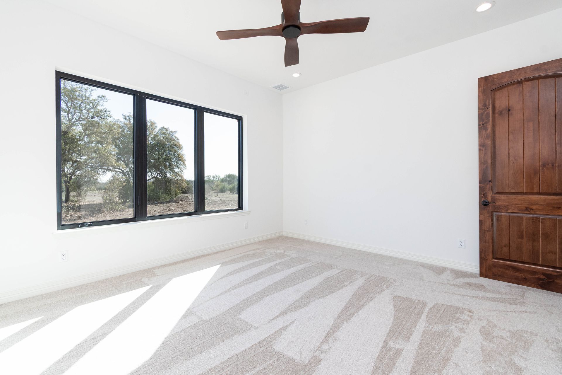 An empty bedroom with three windows and a ceiling fan.
