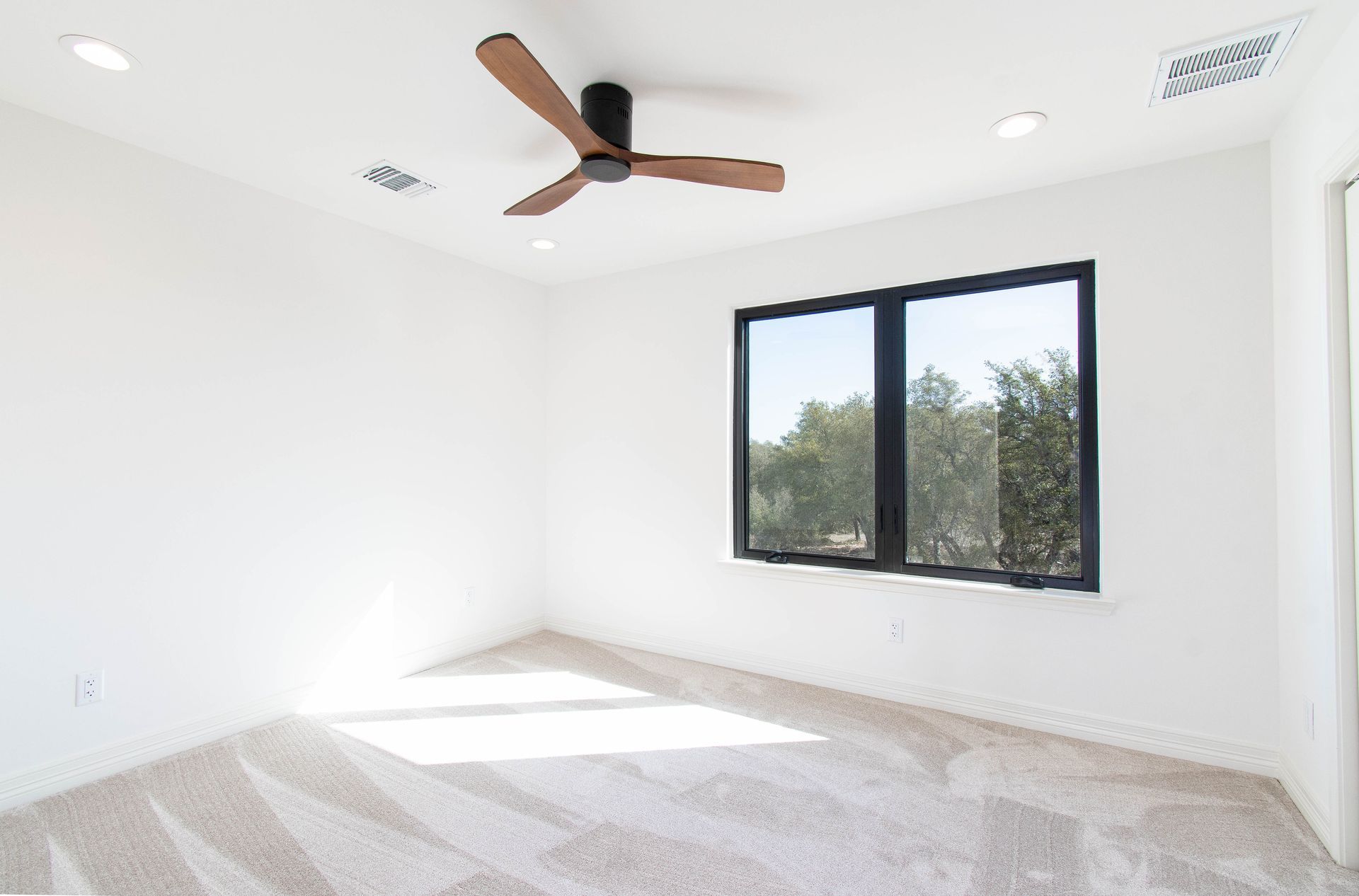 An empty bedroom with a ceiling fan and two windows.