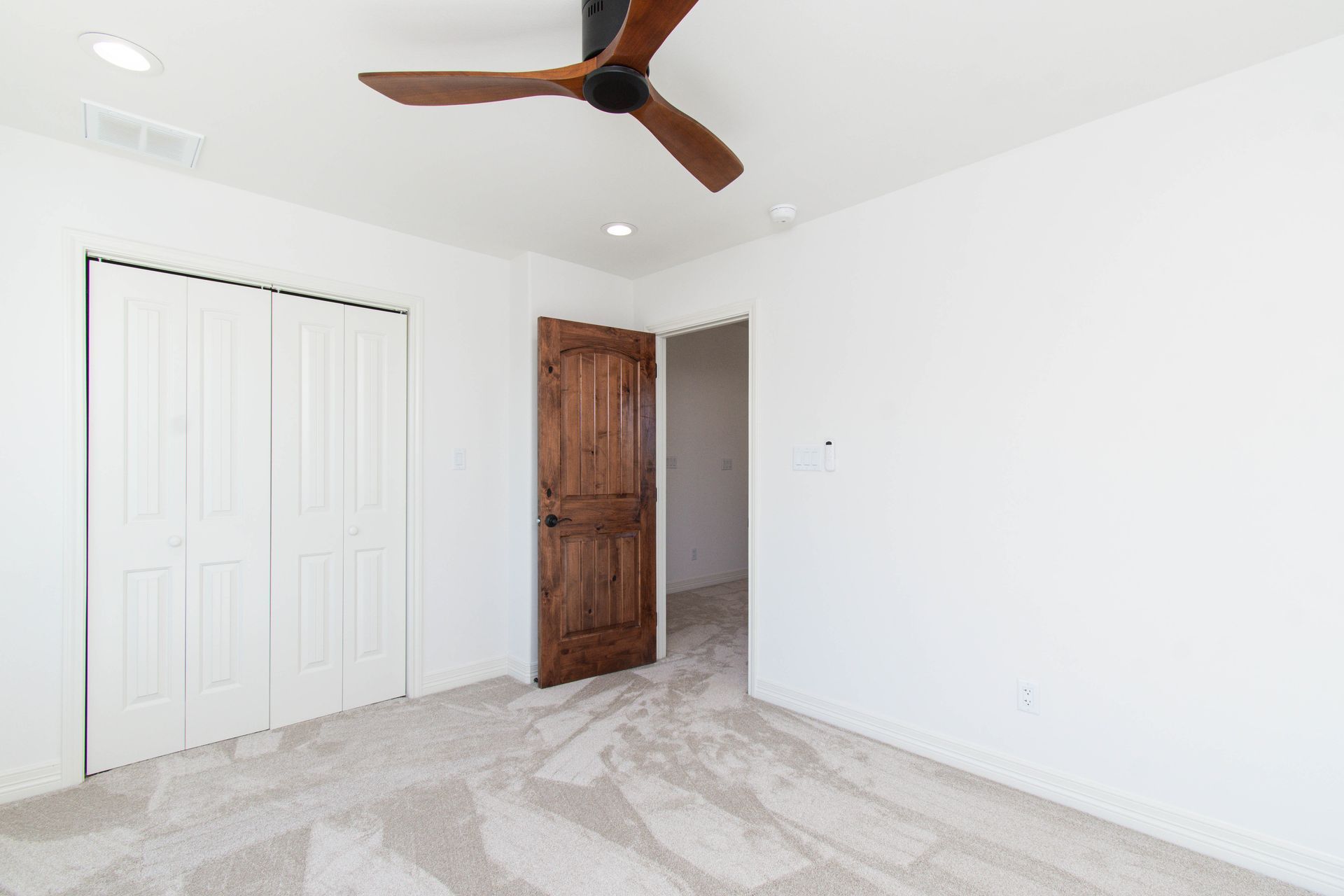 An empty bedroom with a ceiling fan and a wooden door.