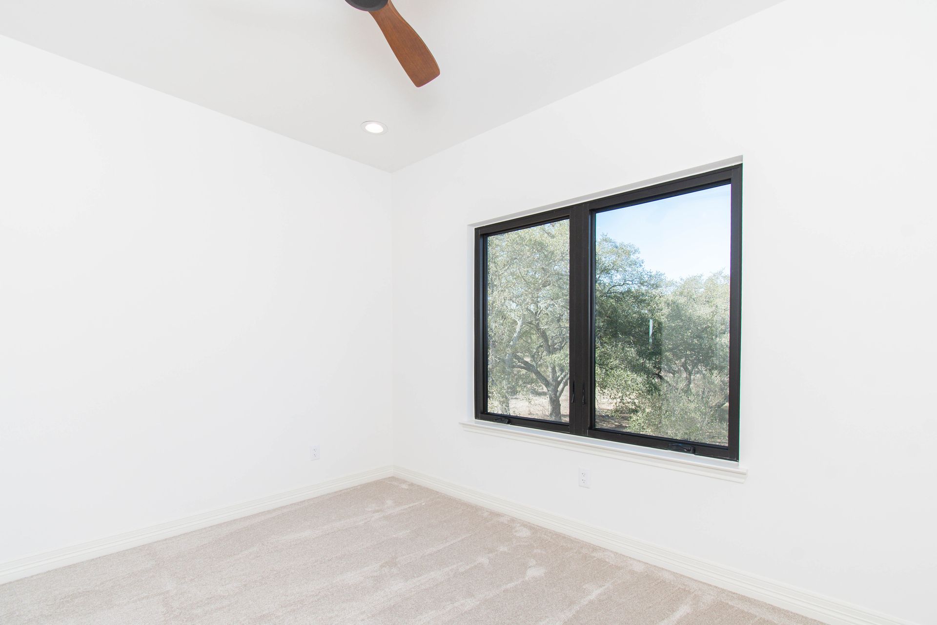 An empty bedroom with two windows and a ceiling fan.