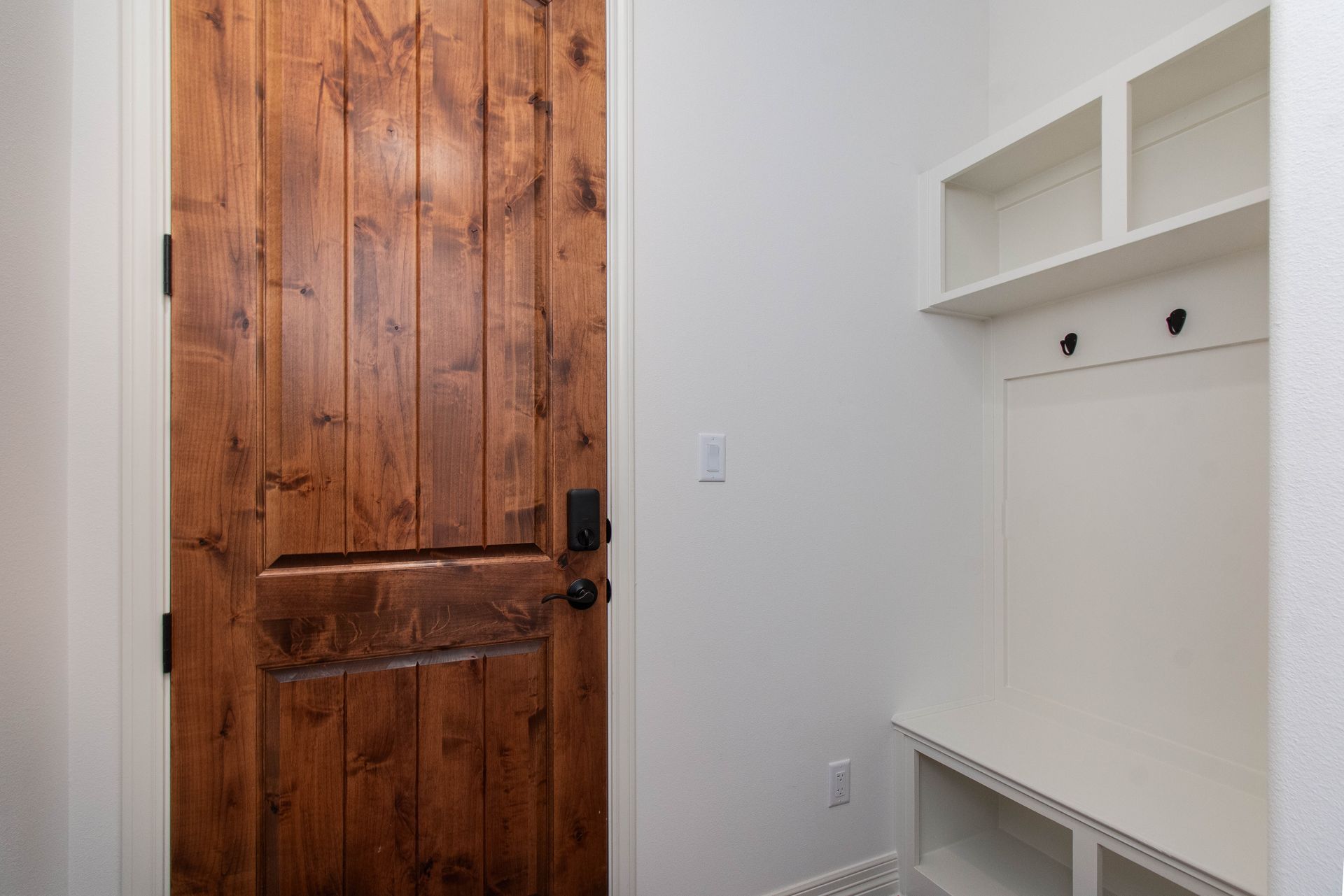 A mud room with a wooden door and white shelves.