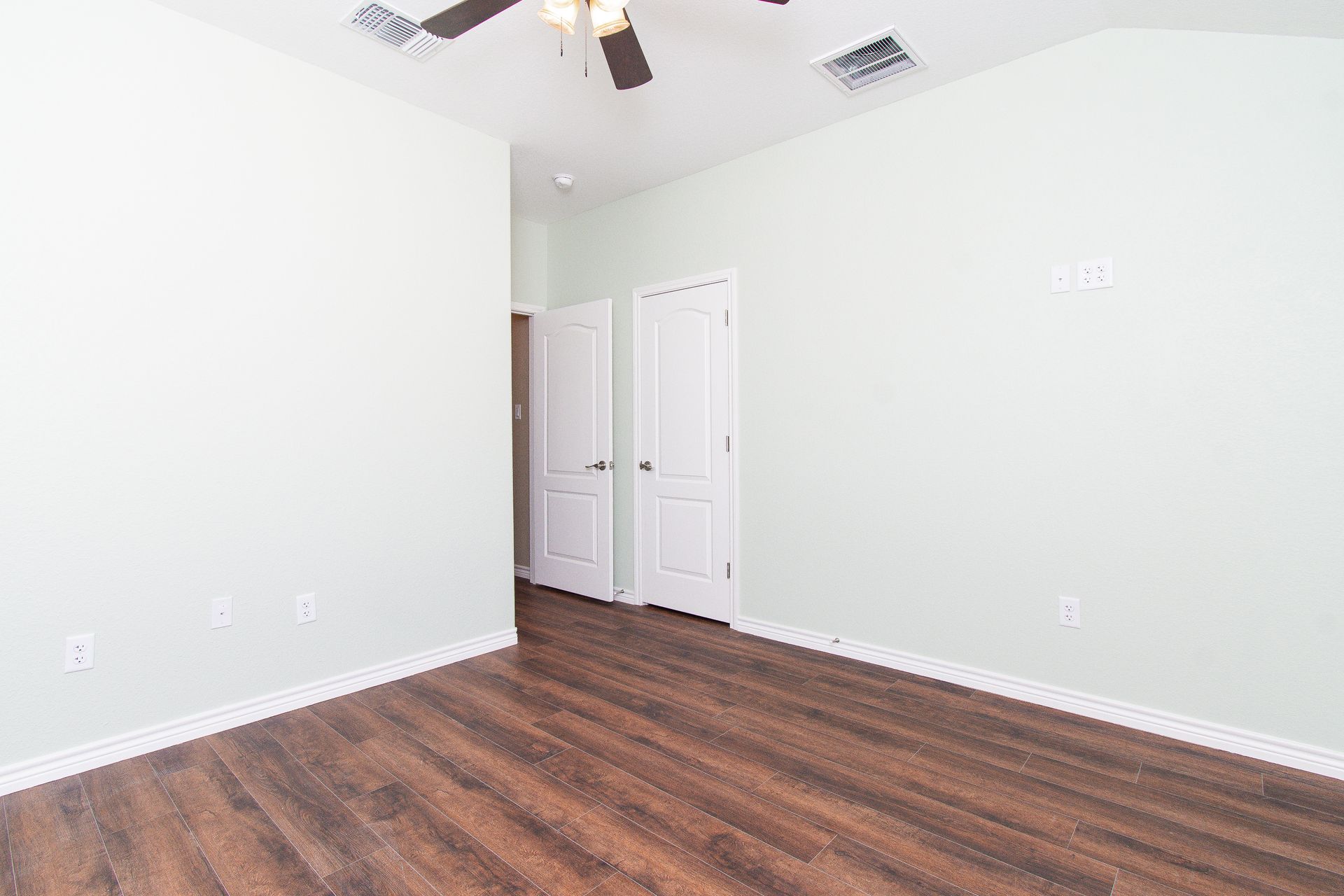An empty bedroom with hardwood floors and a ceiling fan.