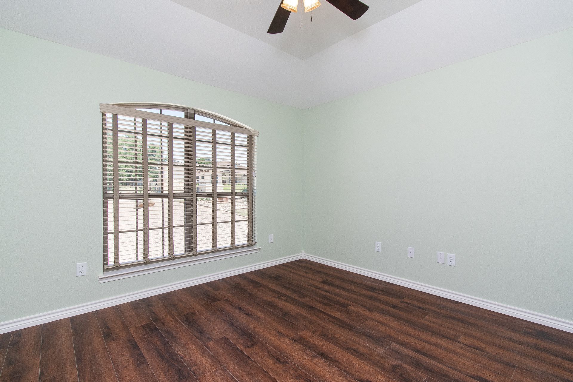 An empty room with hardwood floors and a ceiling fan.