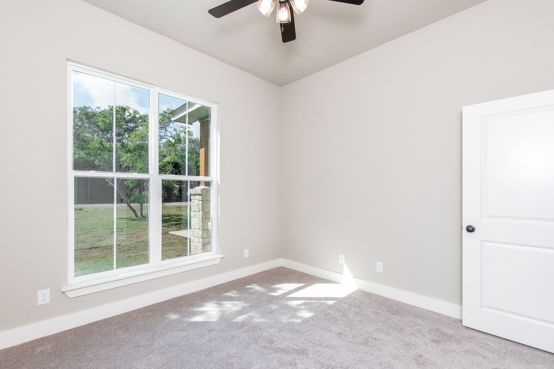 An empty bedroom with two windows and a ceiling fan.
