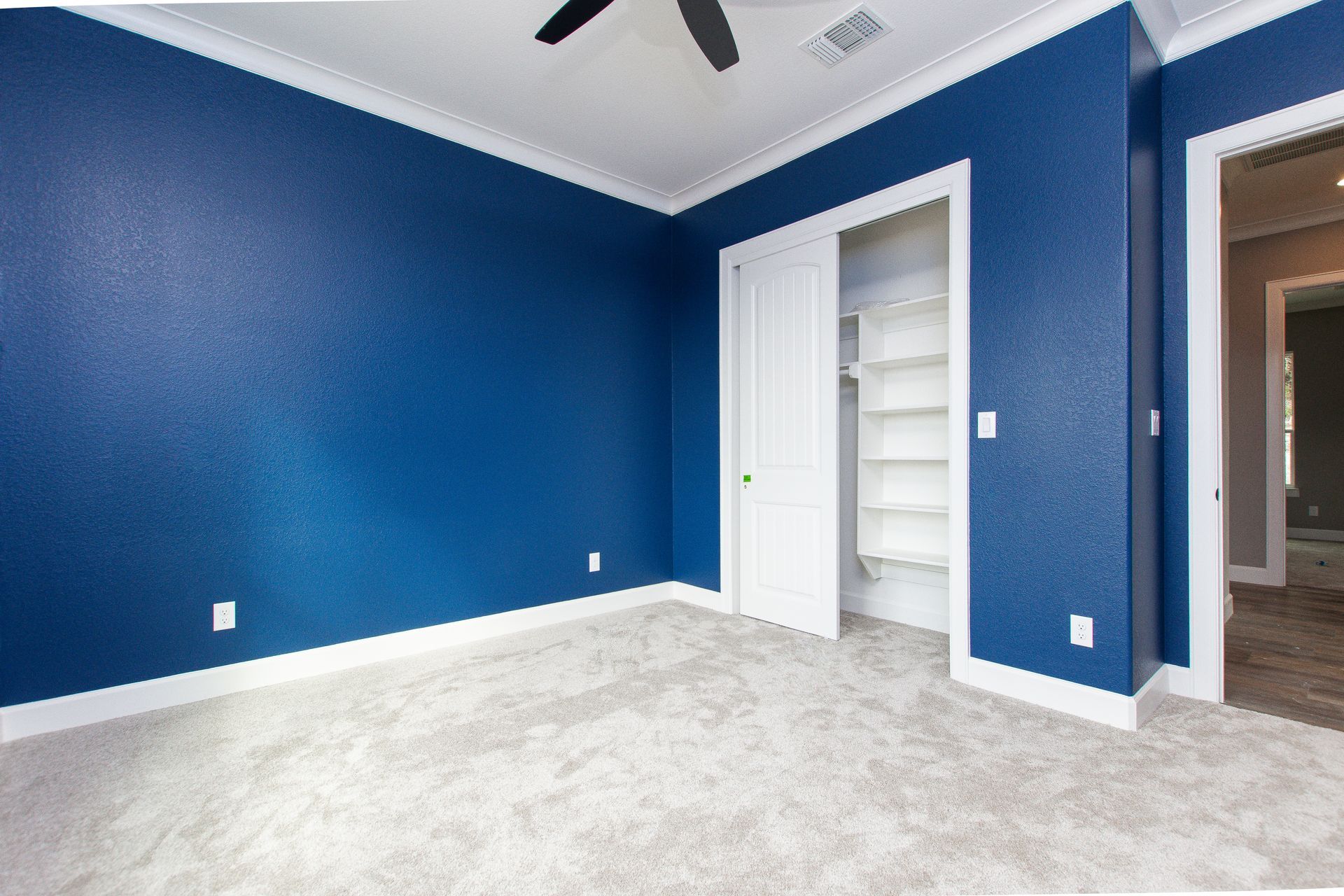 An empty bedroom with blue walls and a ceiling fan