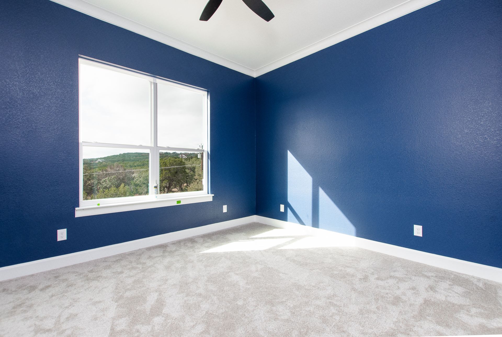 An empty bedroom with blue walls and a ceiling fan