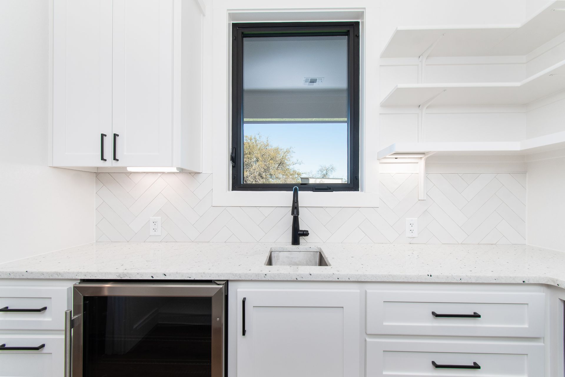 A kitchen with white cabinets , a sink , and a window.