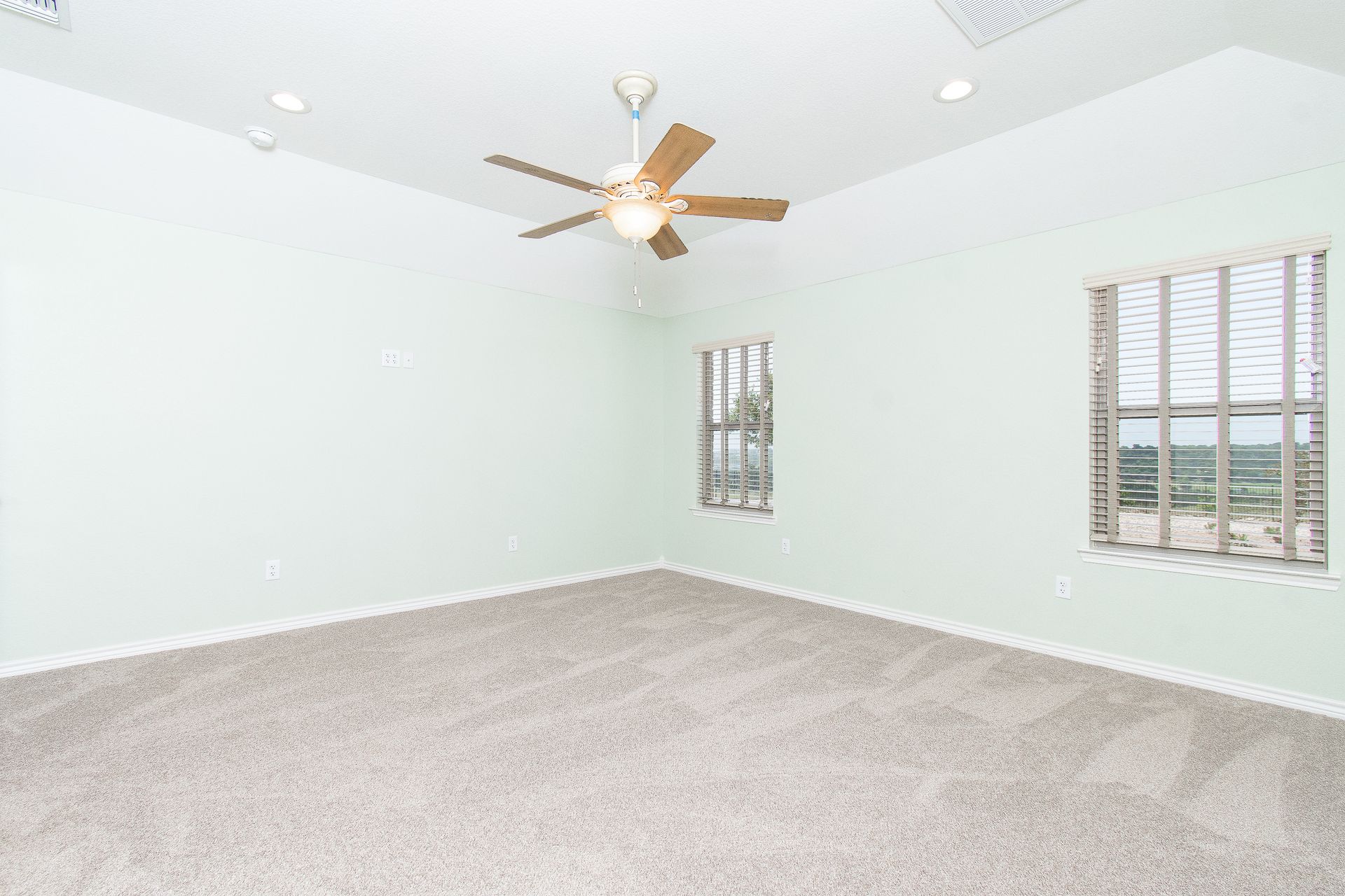 An empty bedroom with a ceiling fan and two windows.