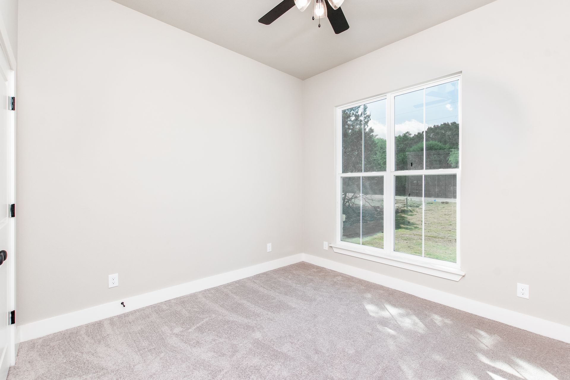 An empty bedroom with a ceiling fan and two windows.