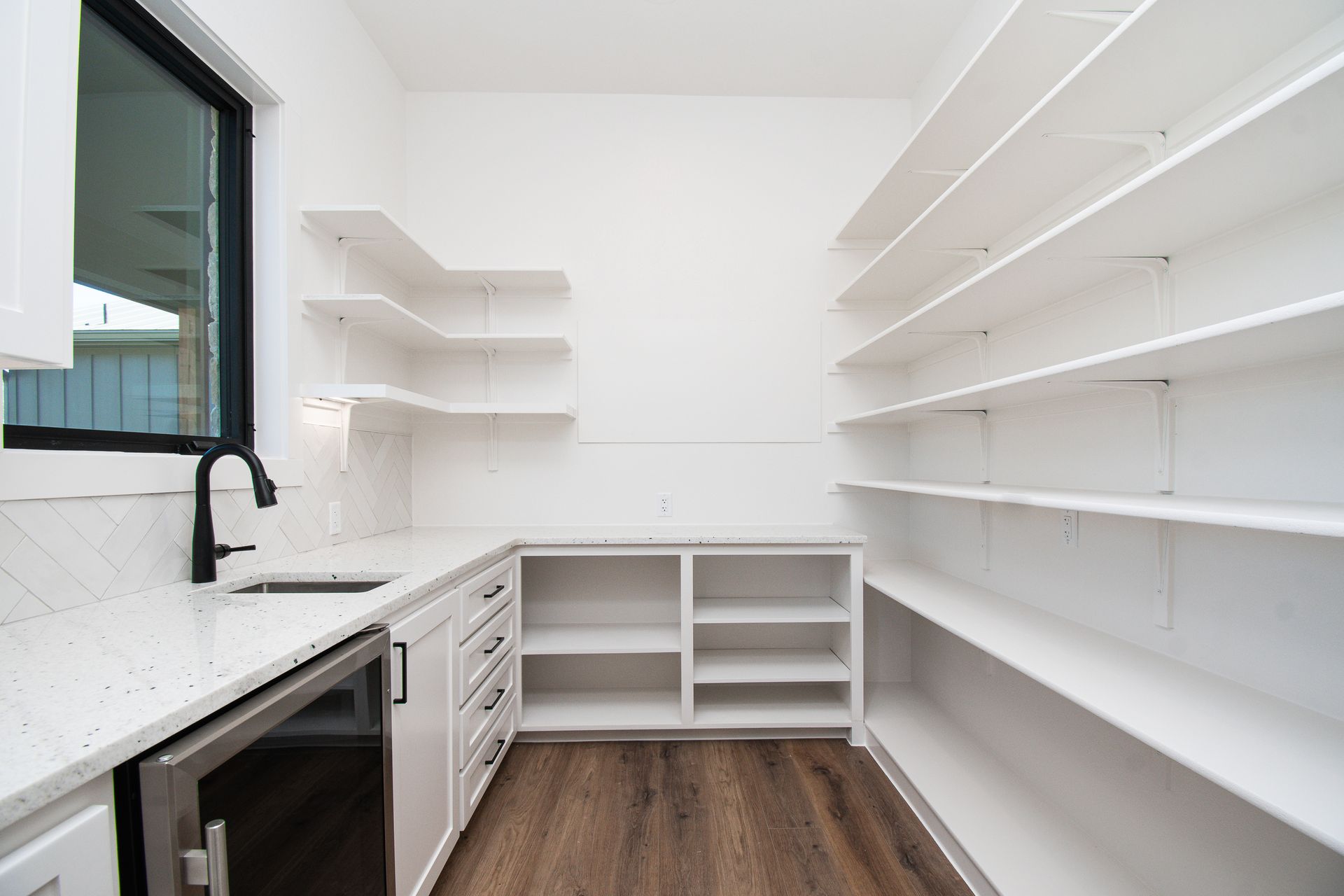 A kitchen with white cabinets , shelves , a sink and a refrigerator.