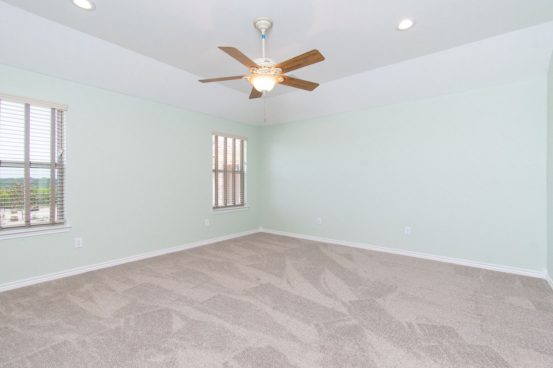 An empty bedroom with a ceiling fan and two windows.