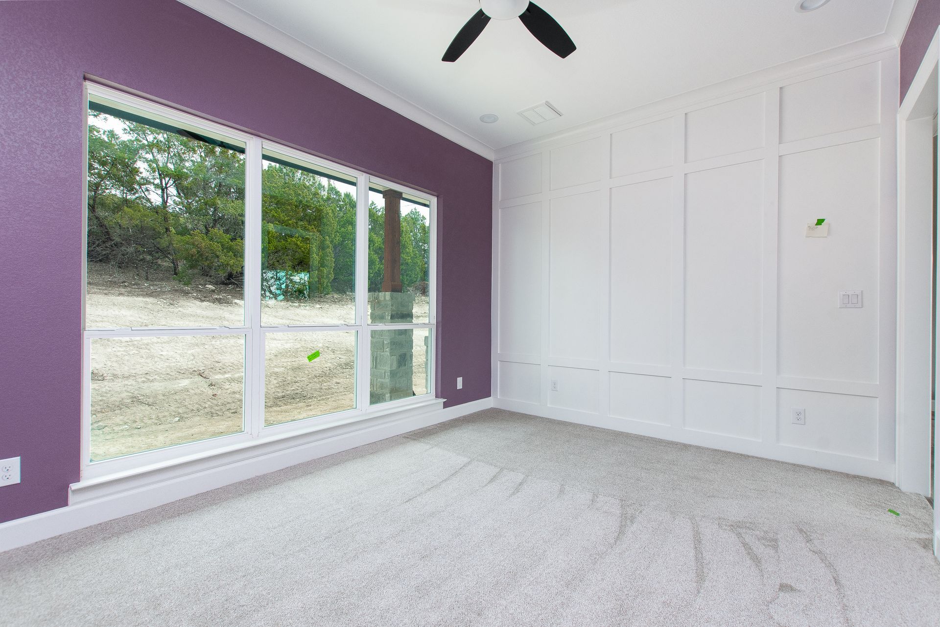 An empty room with purple walls and white trim and a ceiling fan.