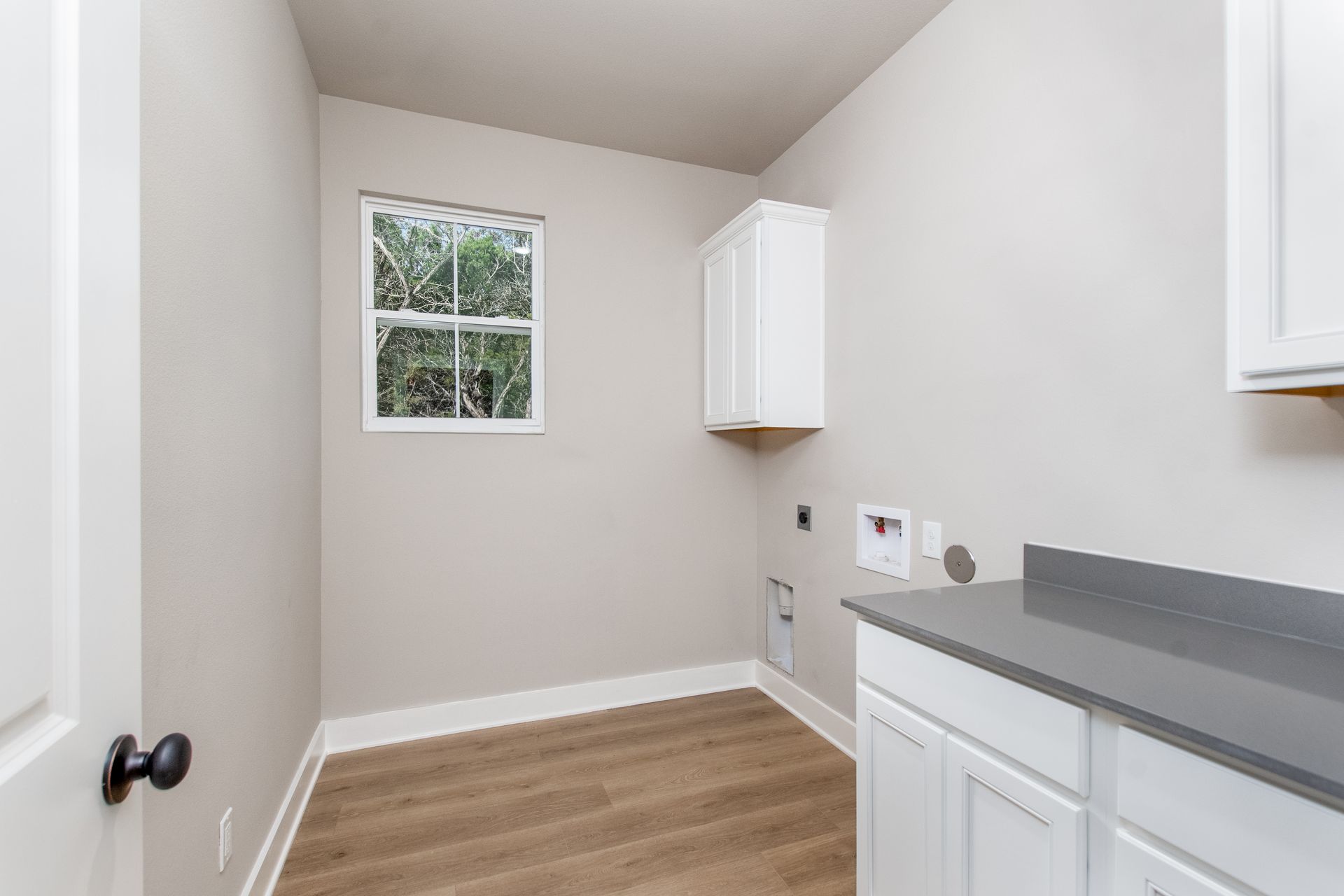 An empty laundry room with white cabinets and a window.