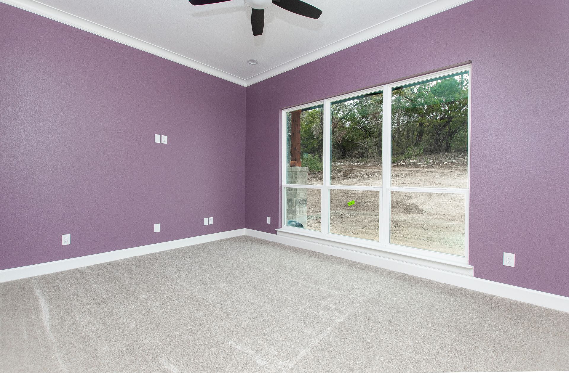 An empty room with purple walls and a ceiling fan.