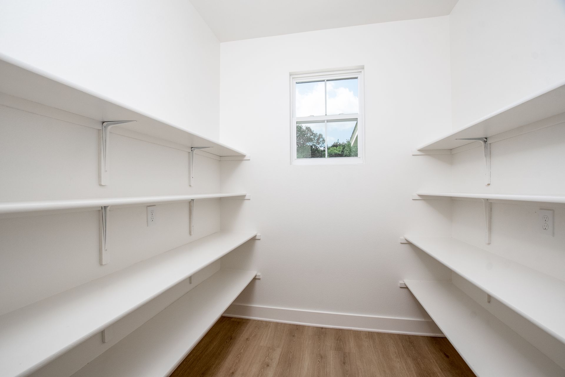 An empty walk in pantry with white shelves and a window.