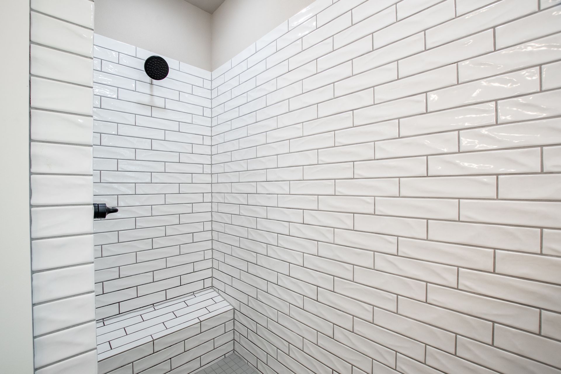A shower with white brick walls and a black shower head.