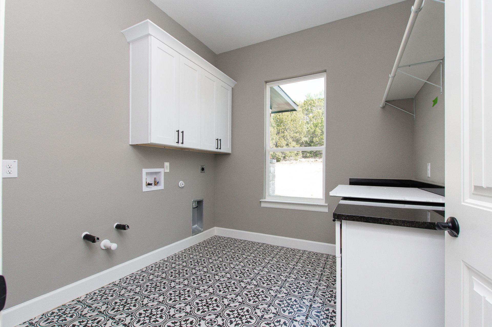 A laundry room with white cabinets and a window.