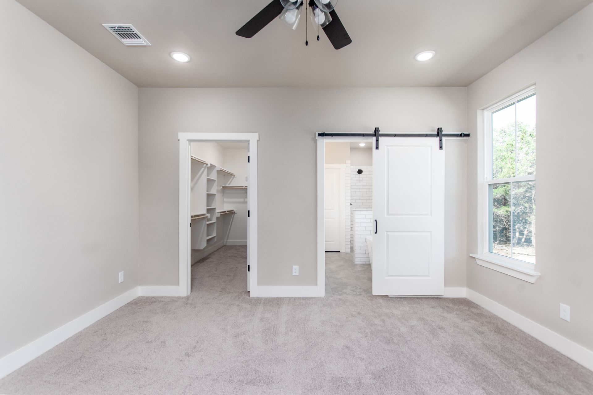 An empty room with a ceiling fan and a sliding barn door