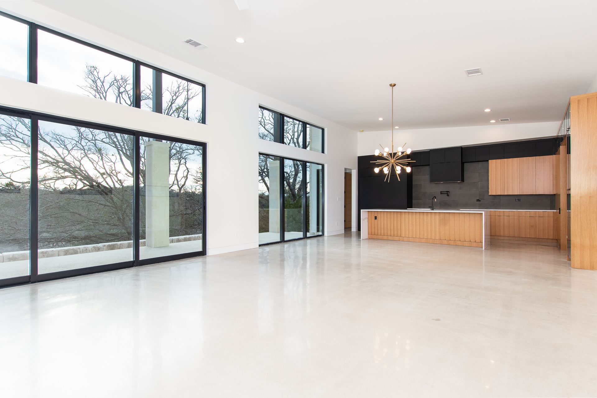 A large empty room with a kitchen and sliding glass doors.