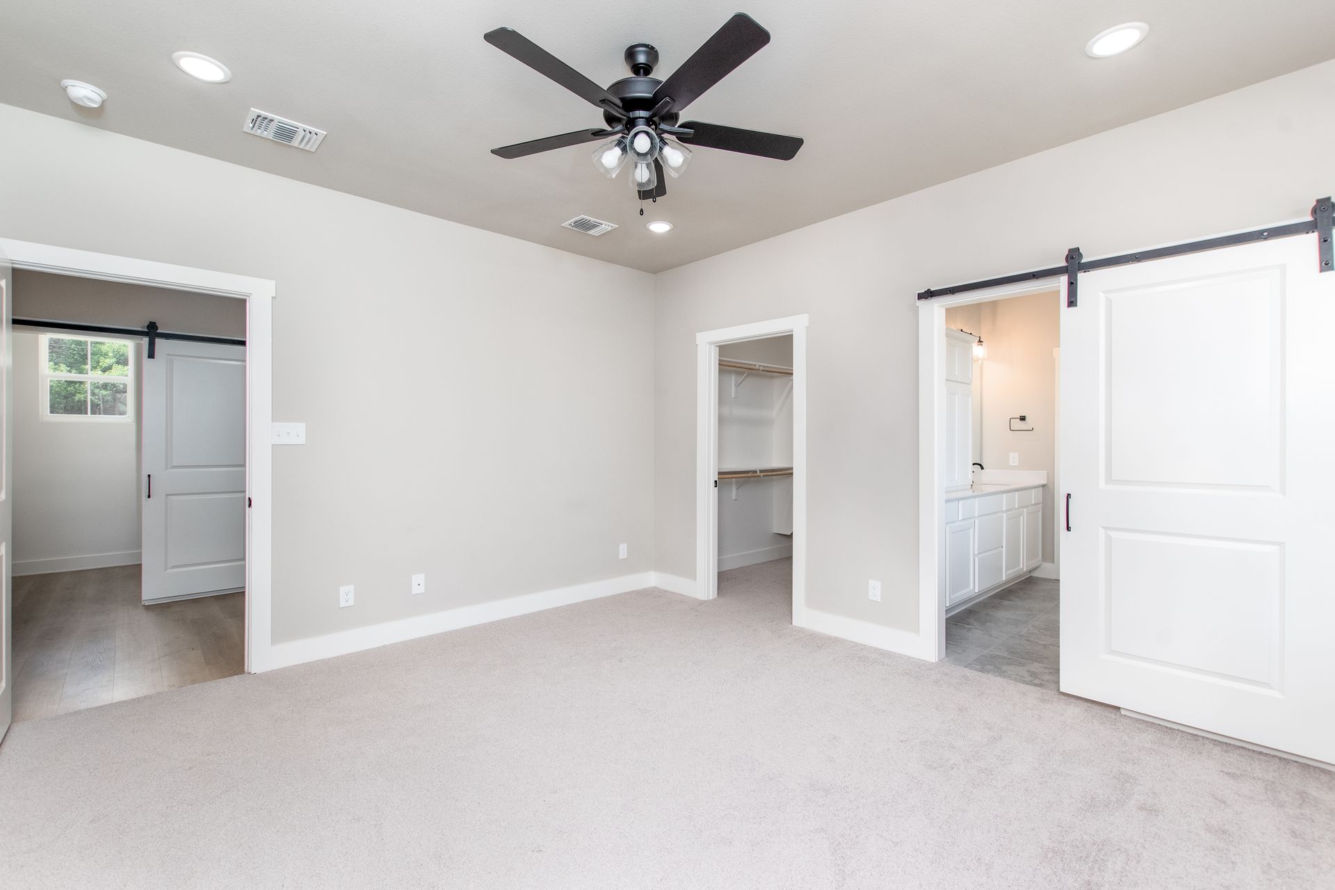 A large empty room with a ceiling fan and sliding barn doors.