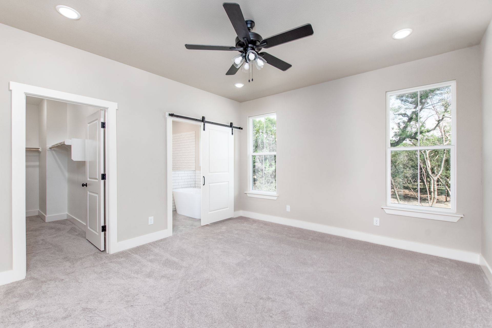 An empty bedroom with a ceiling fan and two windows.