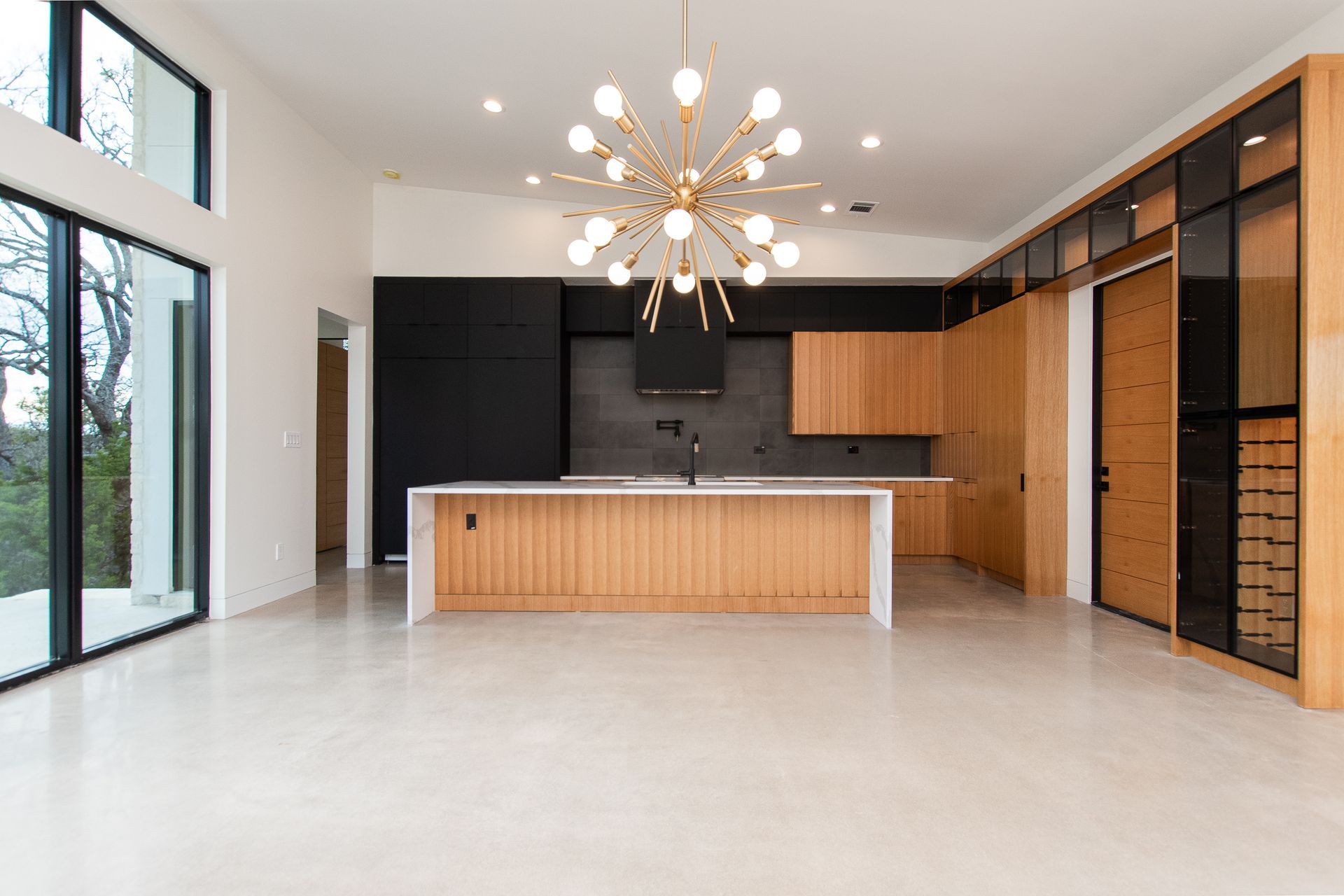 An empty kitchen with a large island and a chandelier hanging from the ceiling.