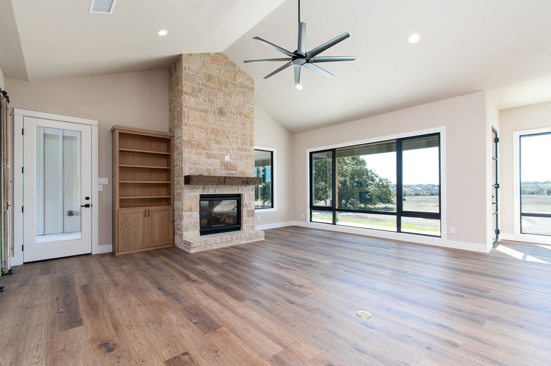 An empty living room with hardwood floors , a fireplace and a ceiling fan.