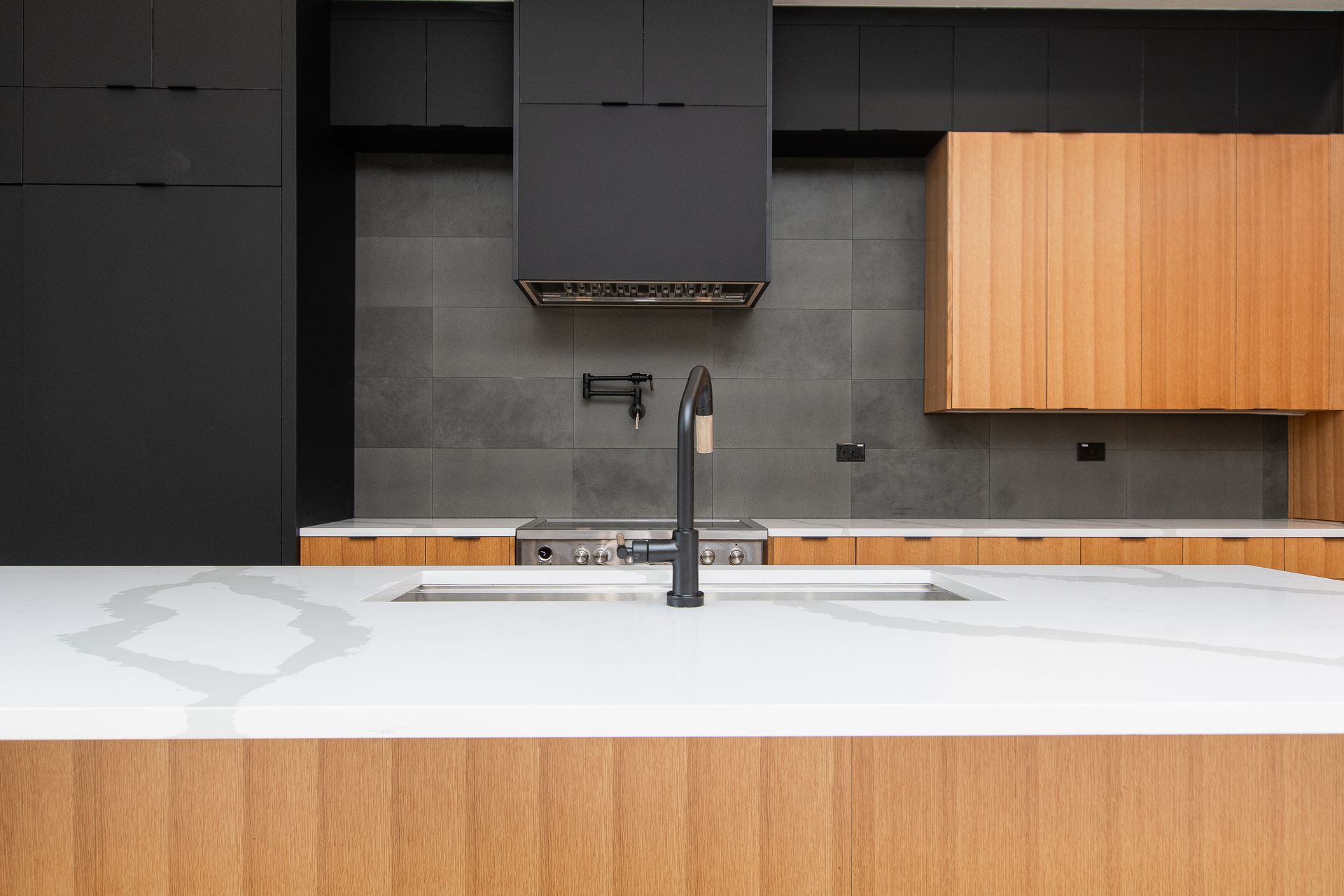 A kitchen with a sink , stove , cabinets and a black faucet.
