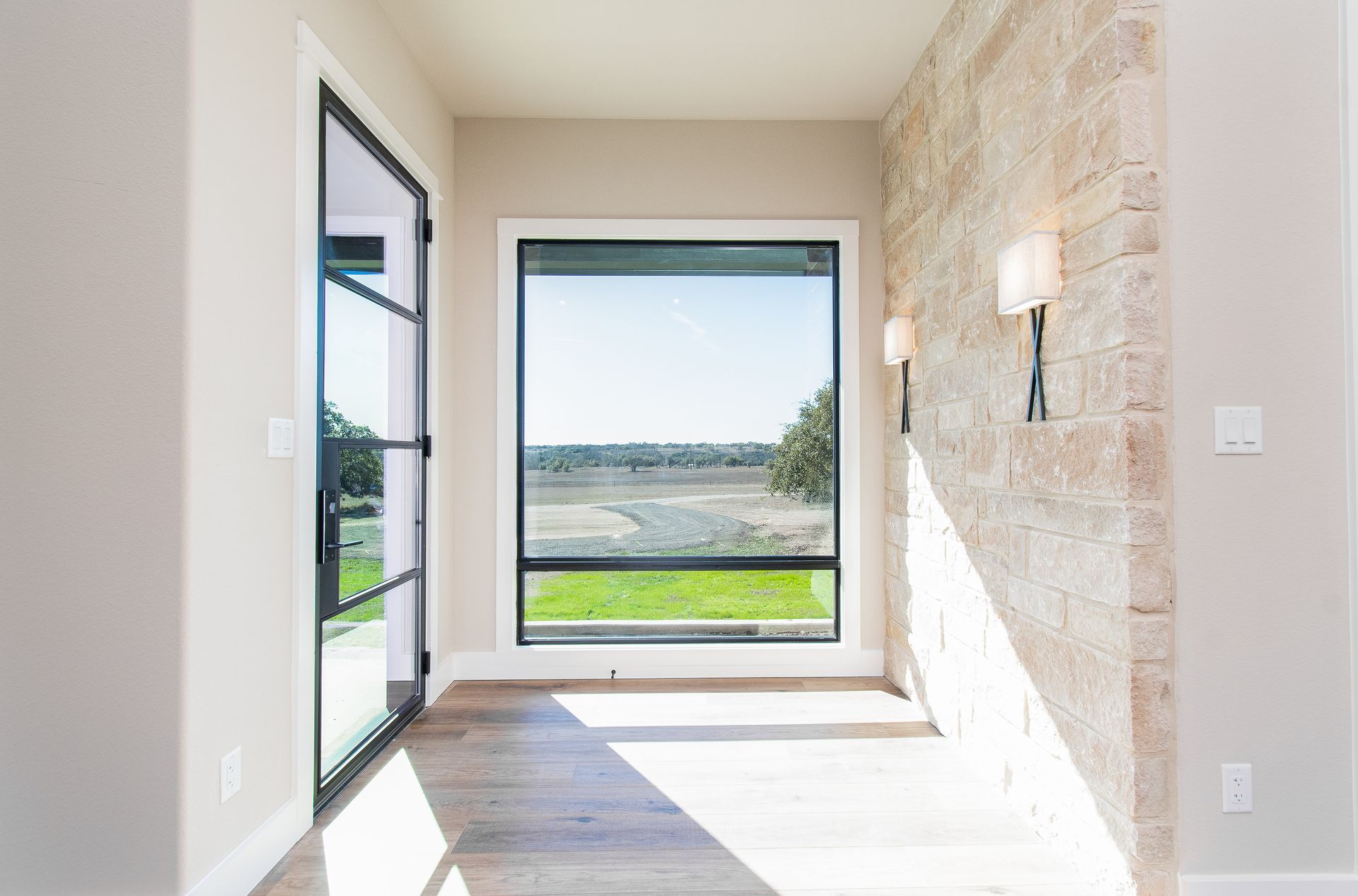 An empty room with a large window and a stone wall.