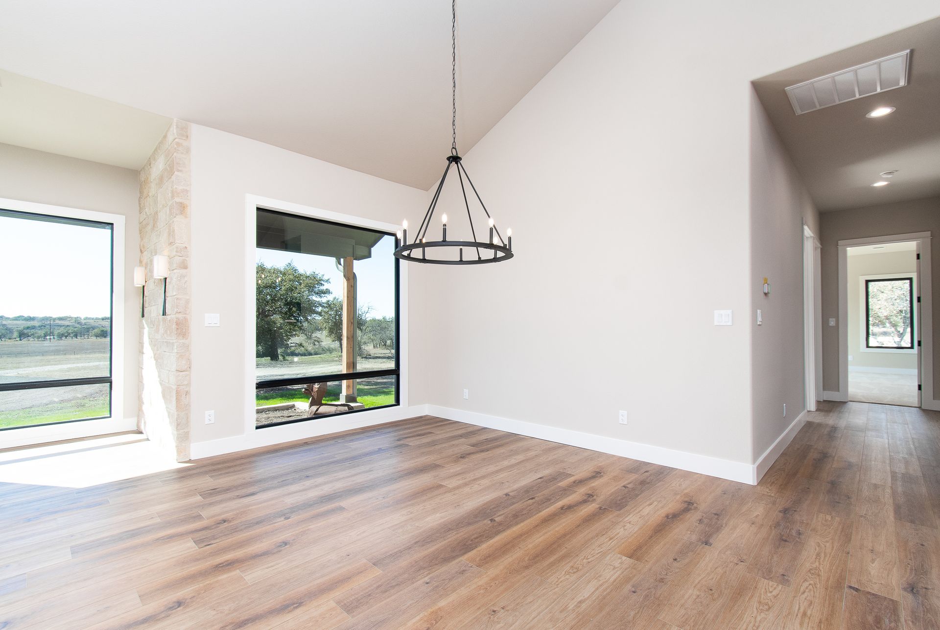 An empty living room with hardwood floors and a chandelier hanging from the ceiling.