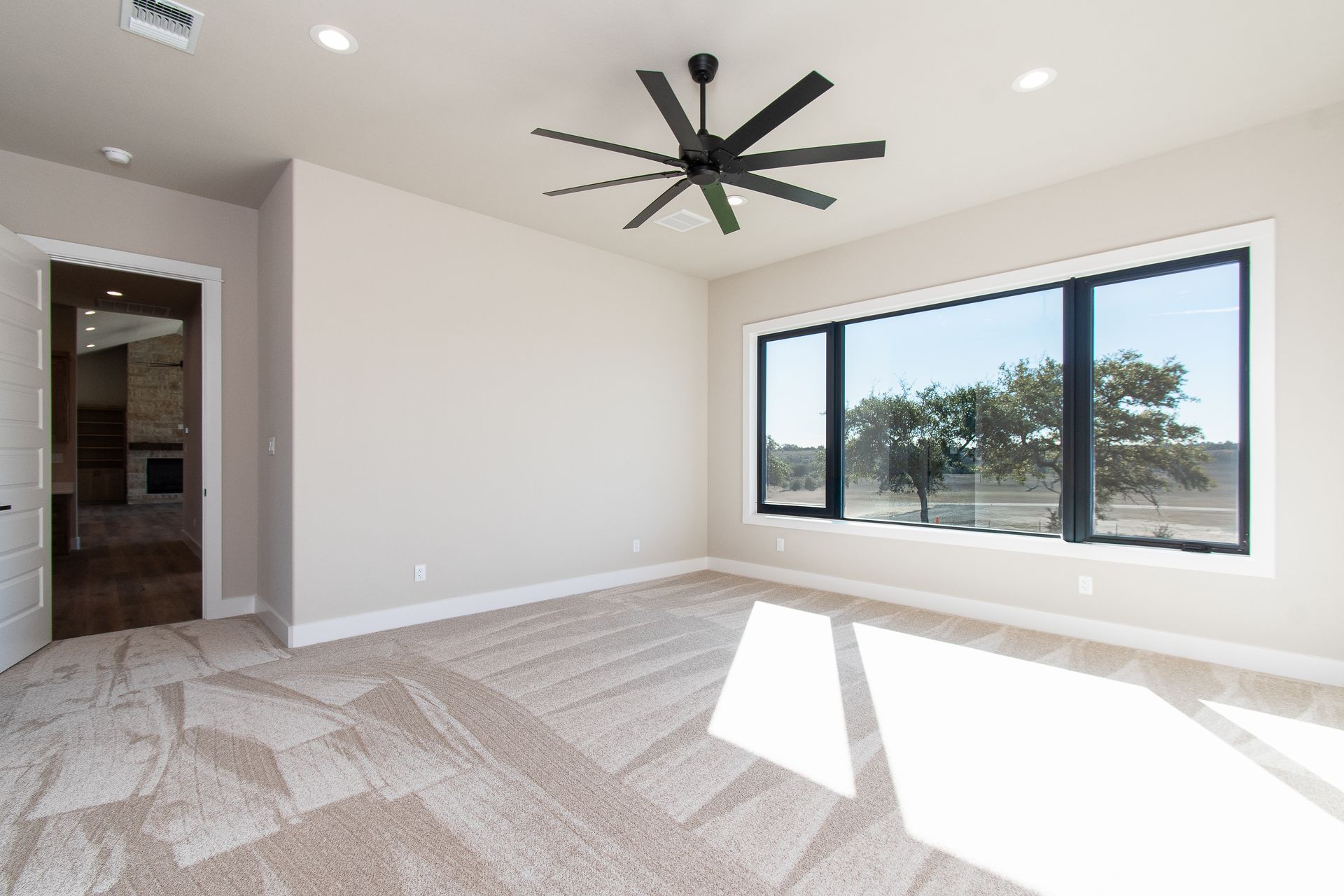An empty room with a large window and a ceiling fan.