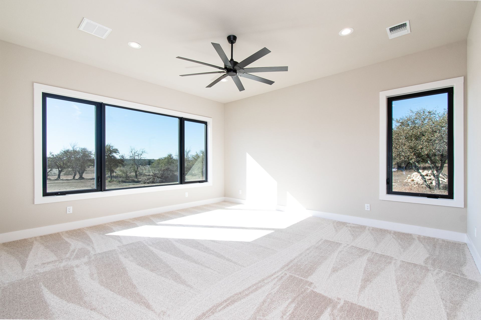 An empty room with a ceiling fan and two windows