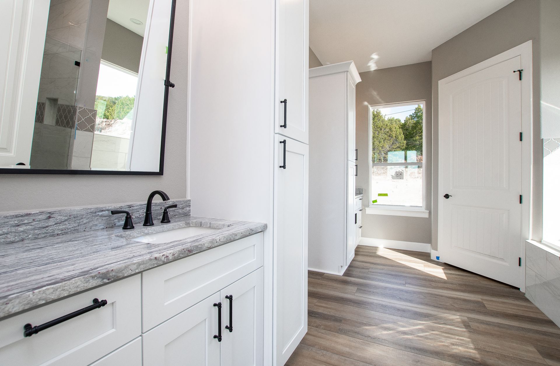 A bathroom with a sink , mirror , cabinets and hardwood floors.