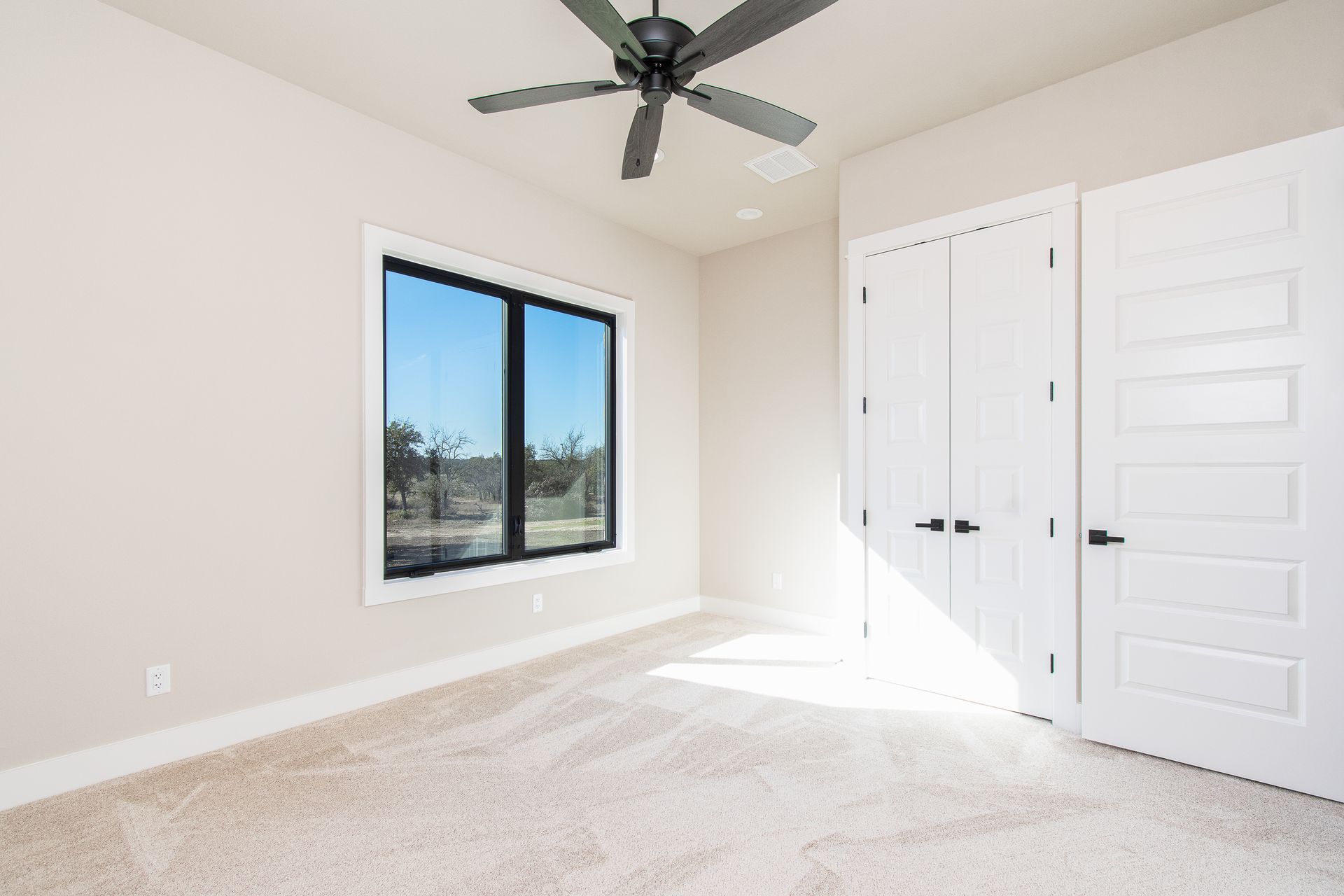 An empty bedroom with a ceiling fan and two windows.