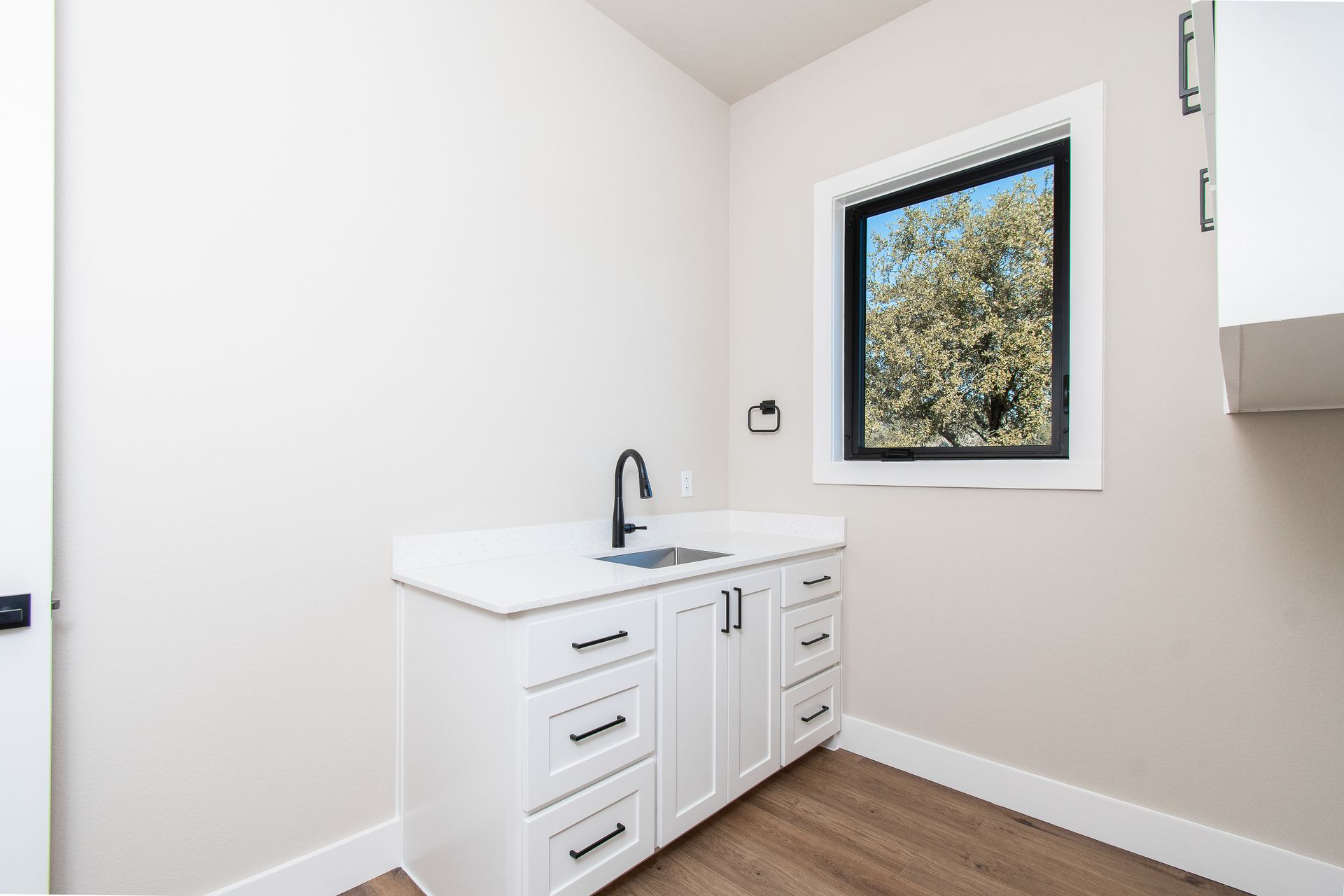 A kitchen with white cabinets , a sink , and a window.