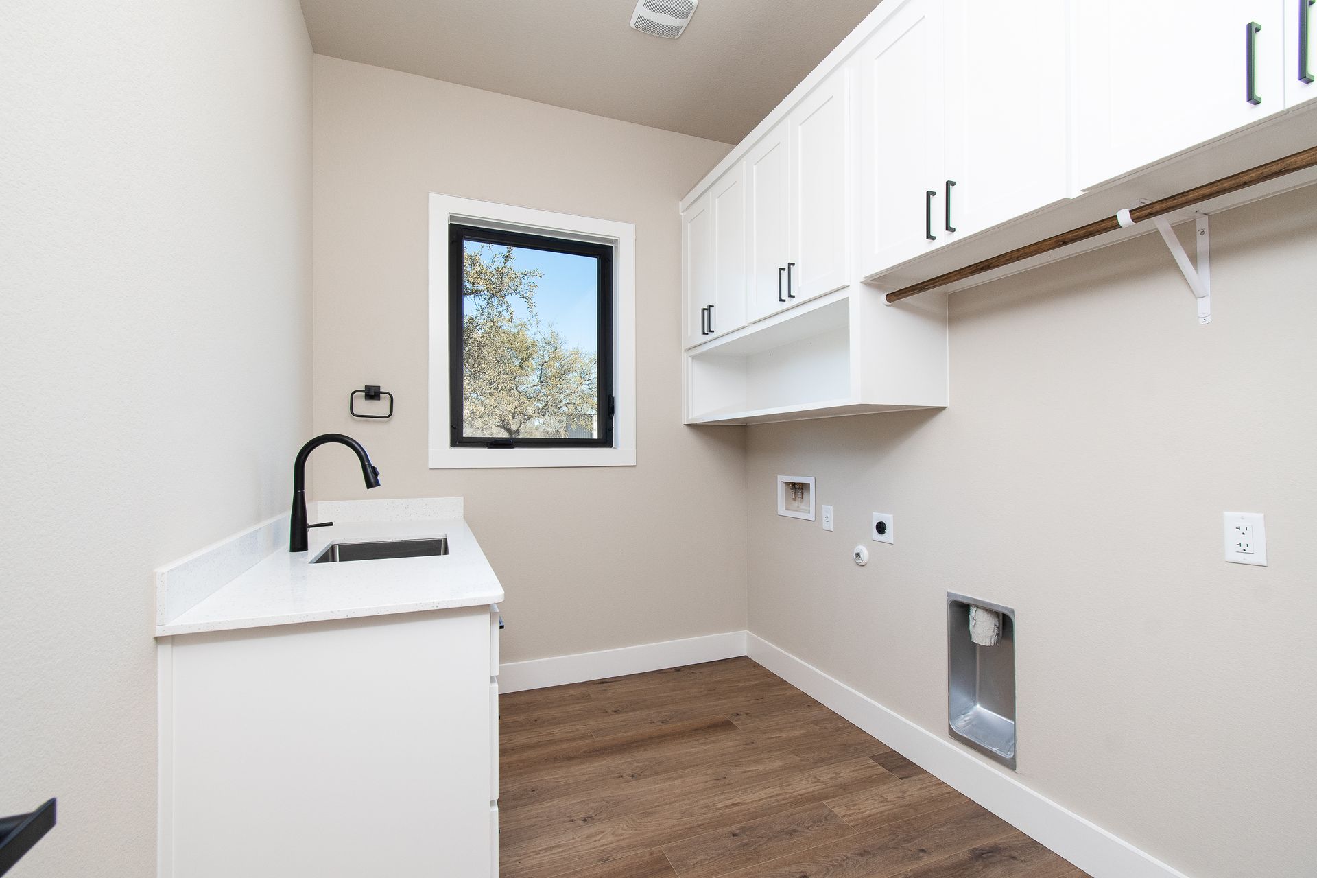 A laundry room with a sink , cabinets , and a window.