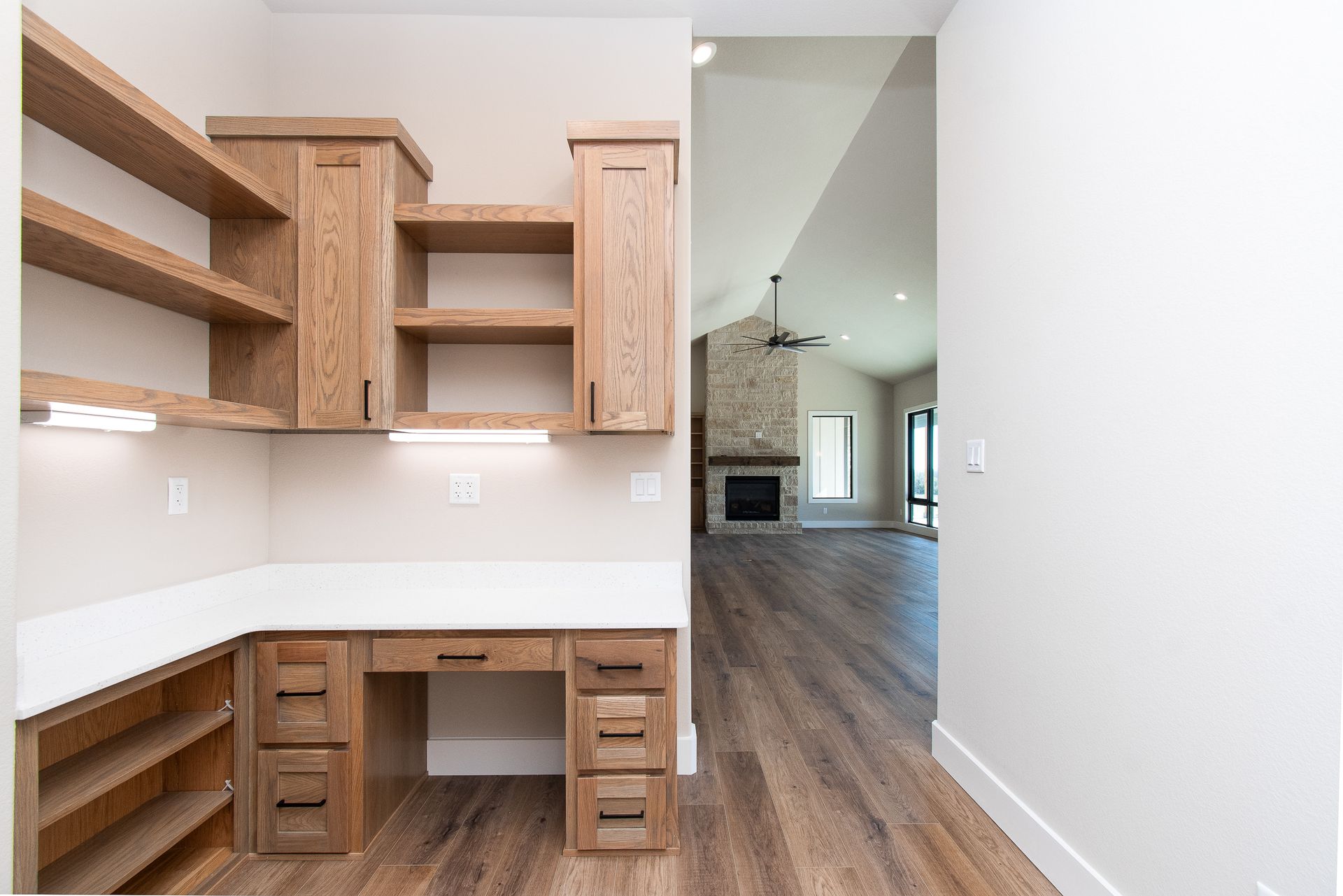 A home office with a desk and shelves in a hallway leading to a living room.