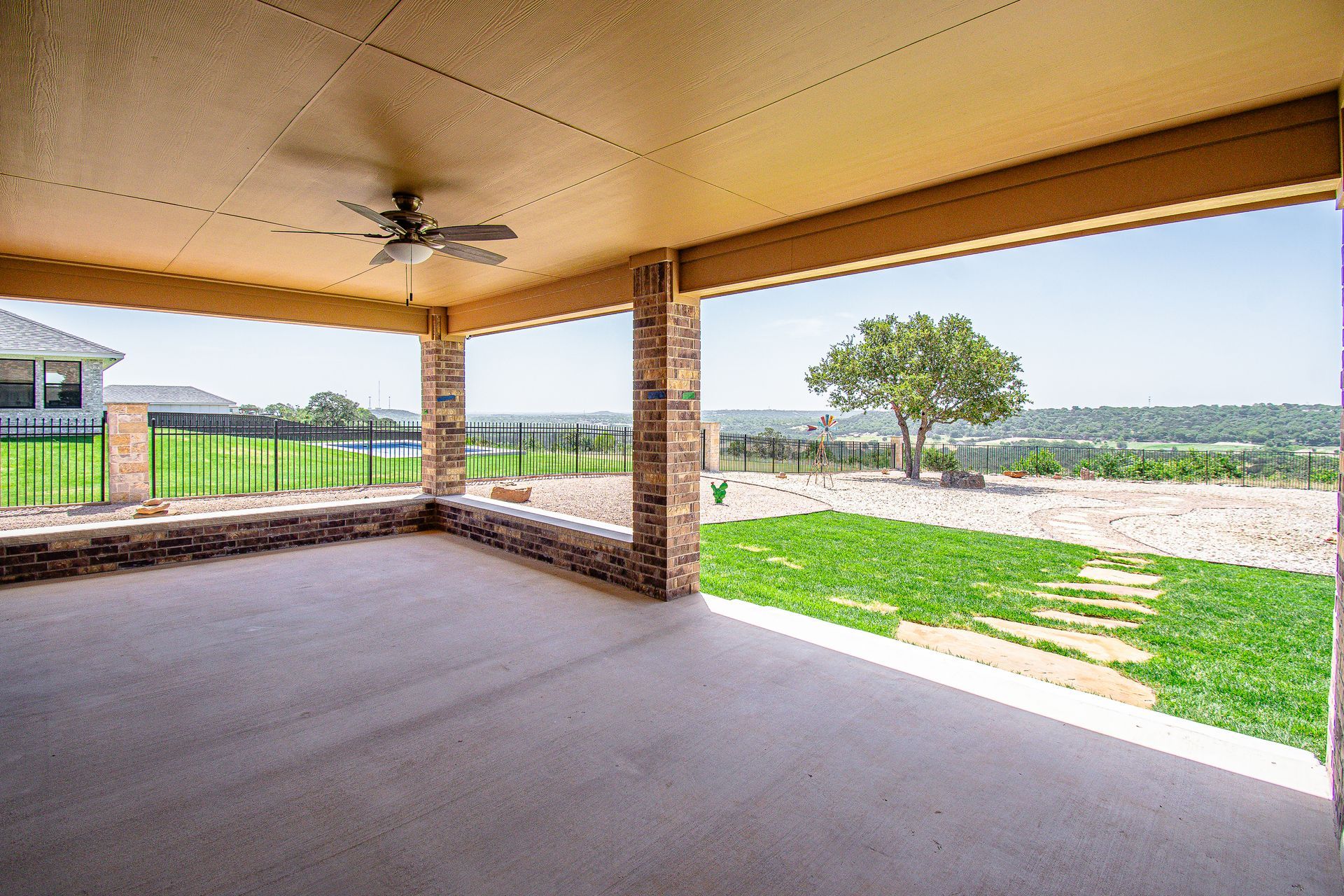 An empty patio with a ceiling fan and a view of a lush green field.