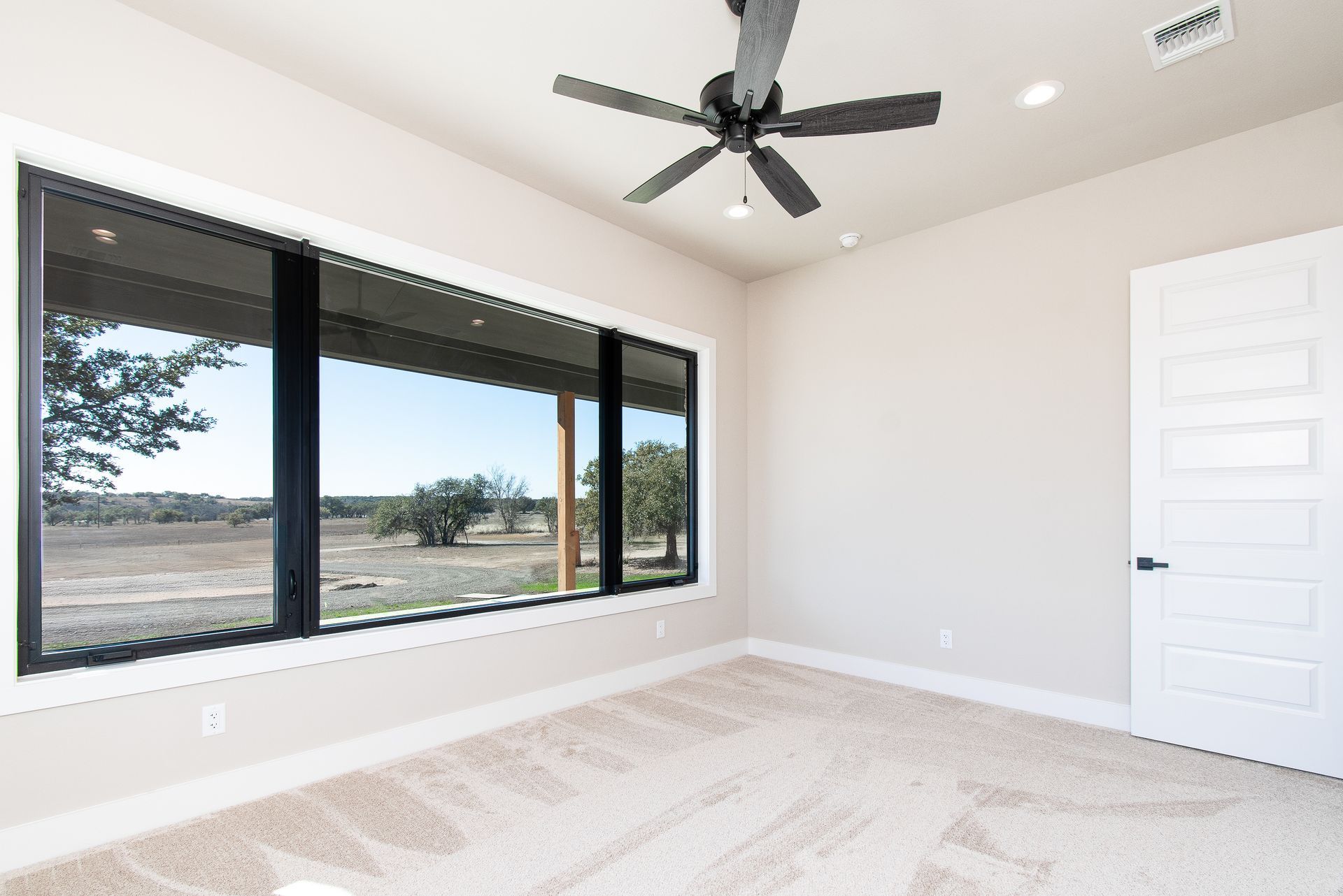 An empty bedroom with a large window and a ceiling fan.