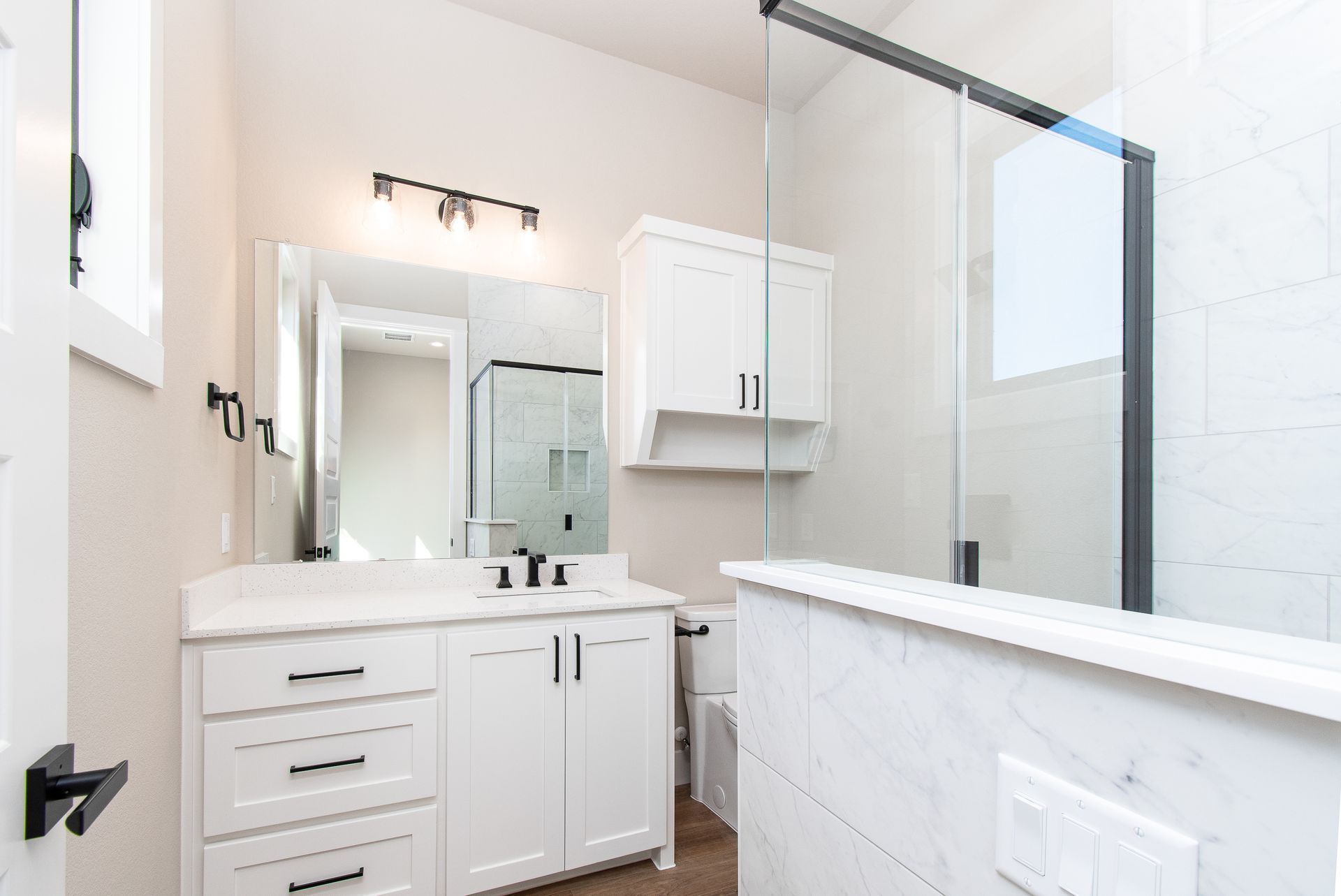 A bathroom with white cabinets , a sink , a mirror and a walk in shower.