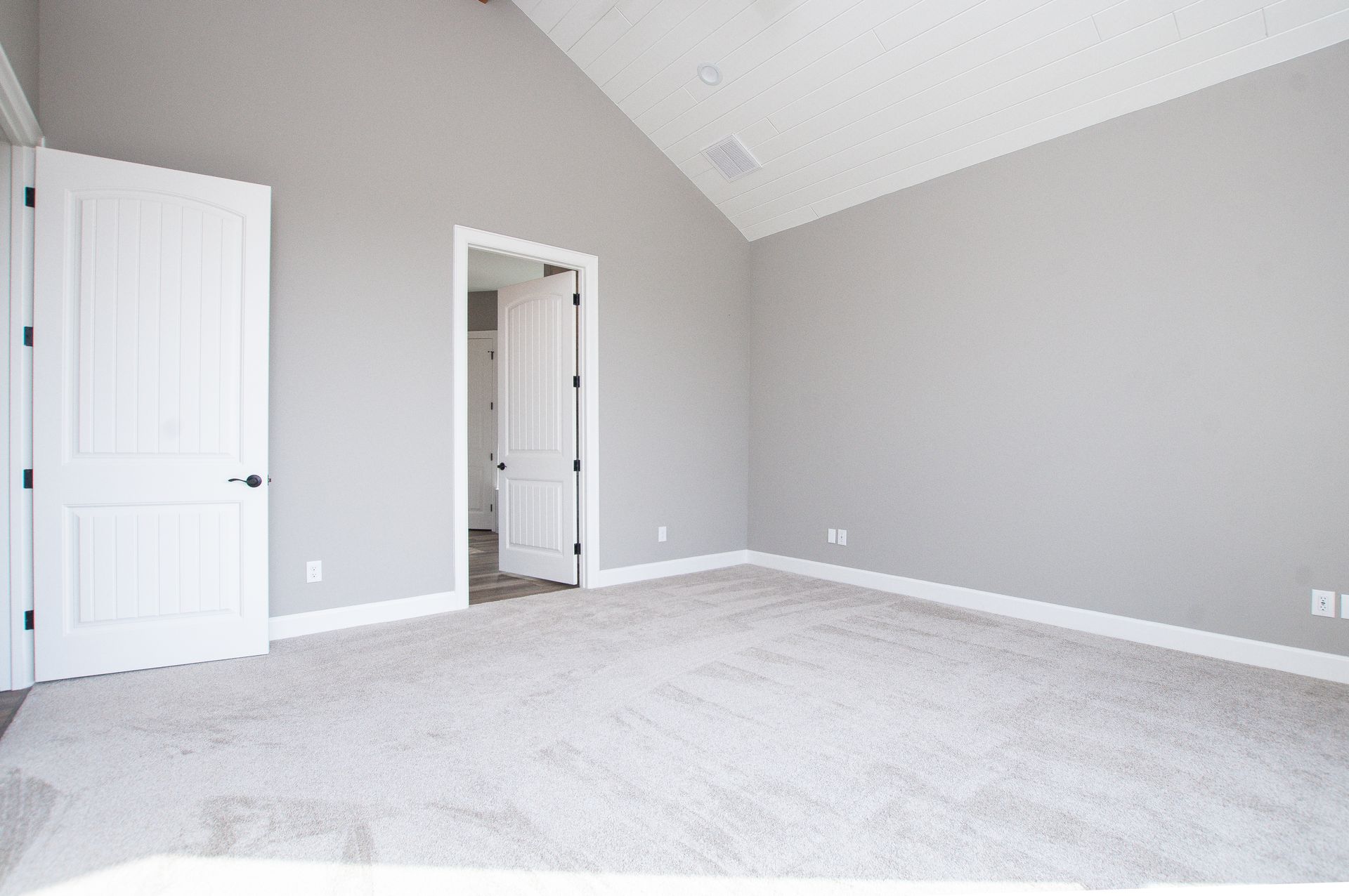 An empty bedroom with gray walls and a vaulted ceiling.