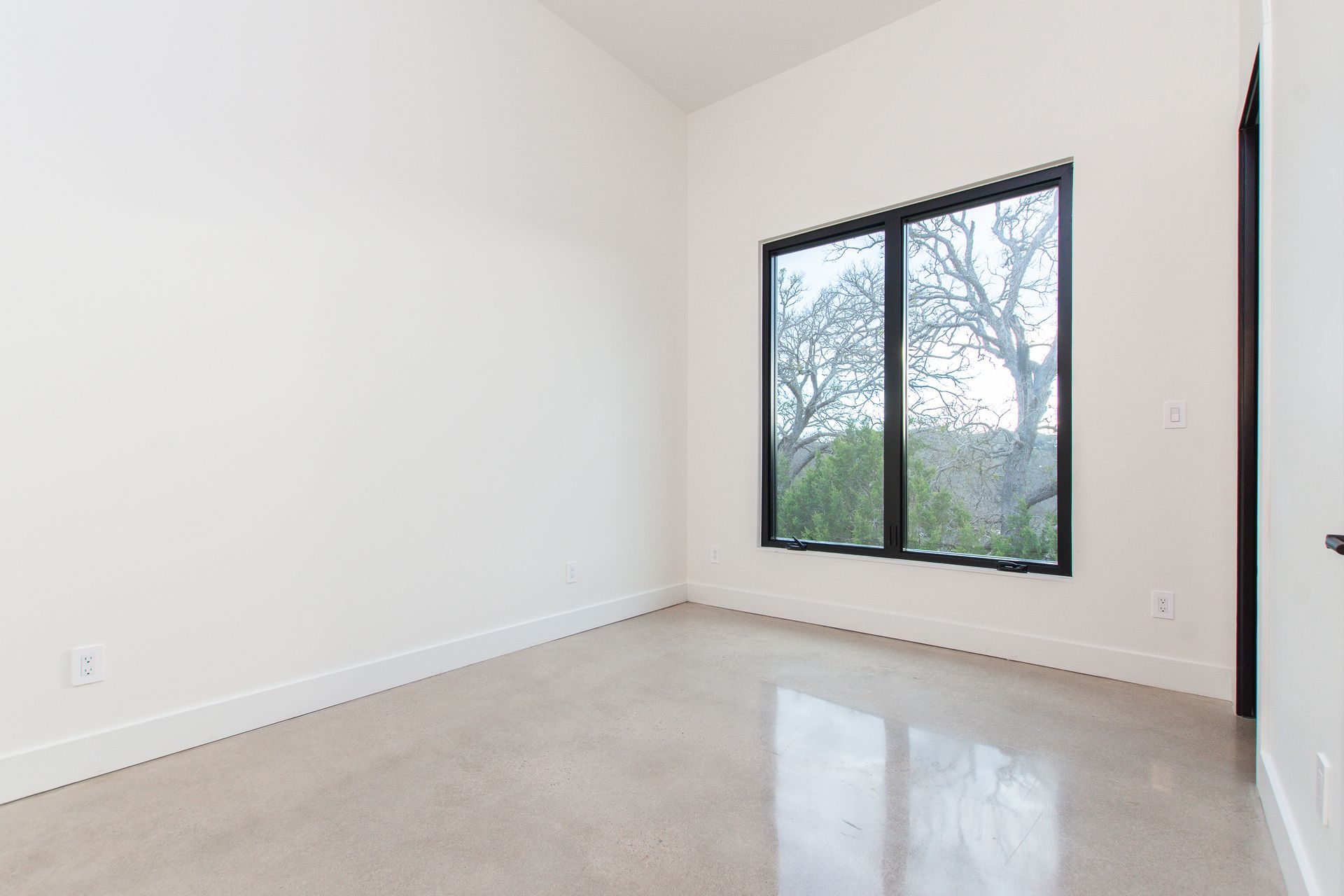 An empty room with two windows and a concrete floor.