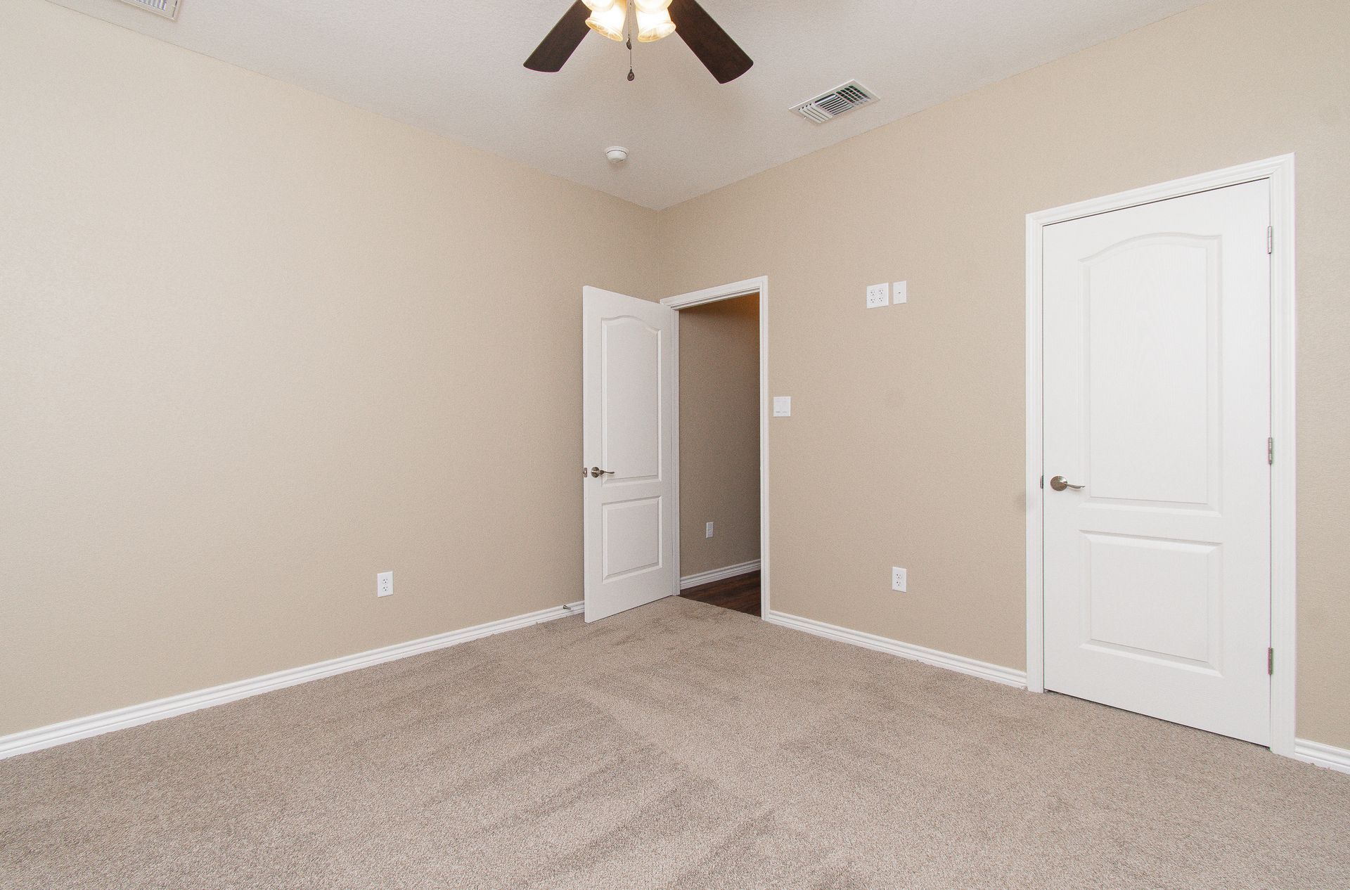 An empty bedroom with a ceiling fan and a carpeted floor.