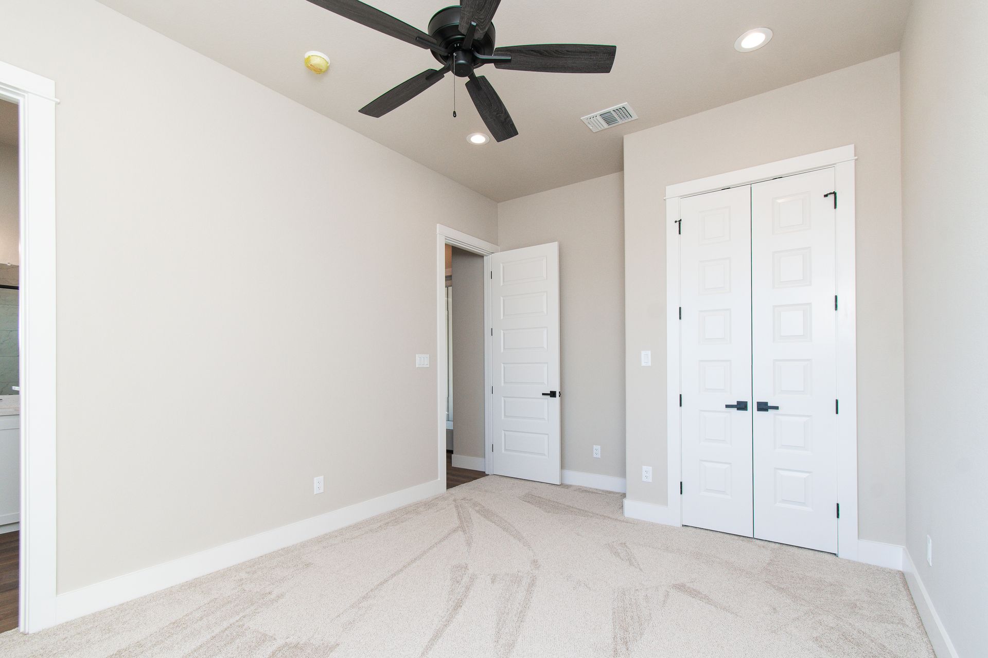An empty bedroom with a ceiling fan and two doors.
