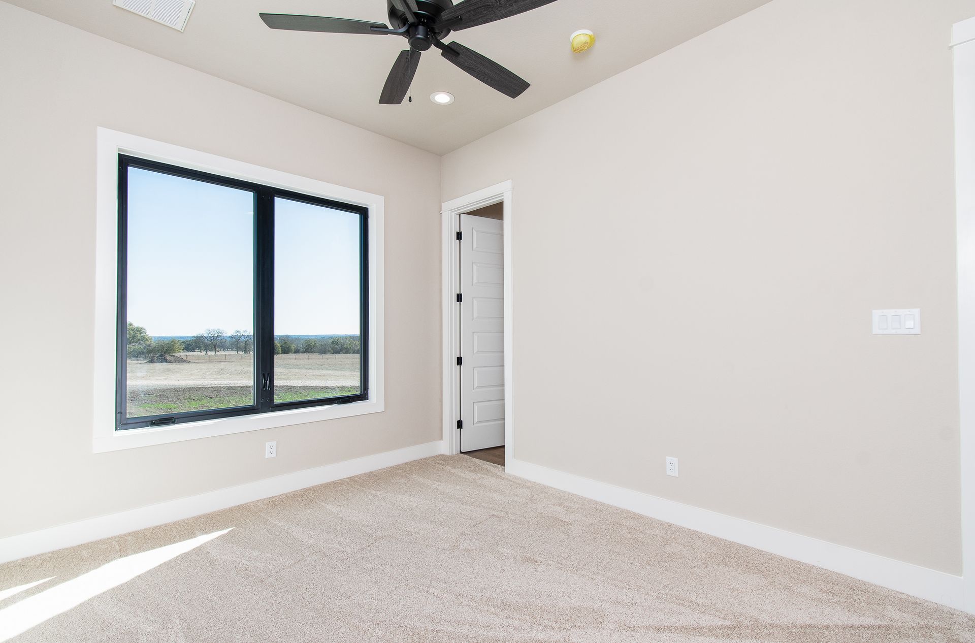 An empty bedroom with two windows and a ceiling fan.