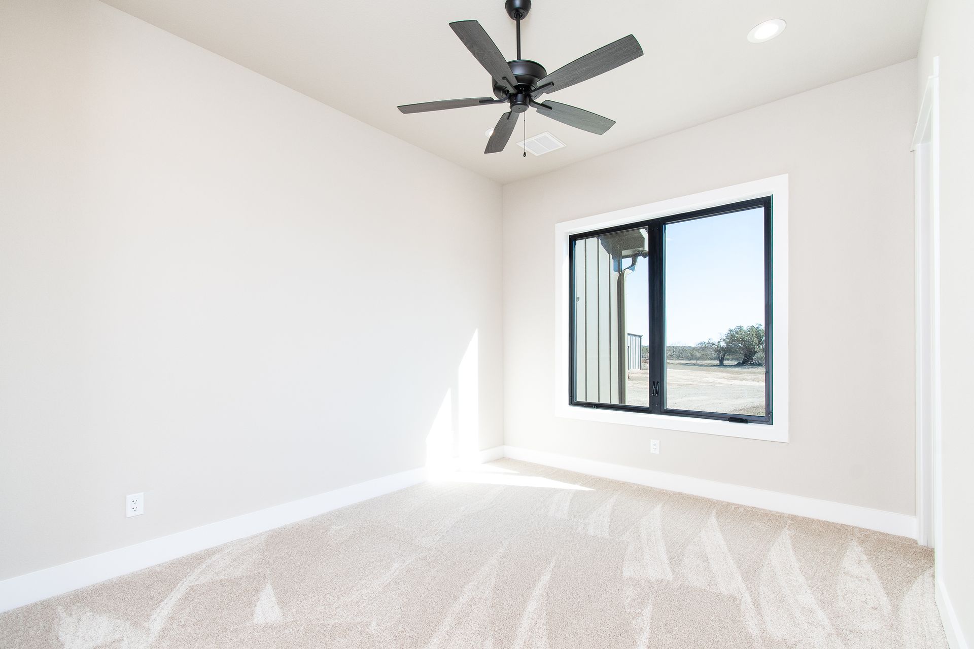 An empty bedroom with a ceiling fan and a window.